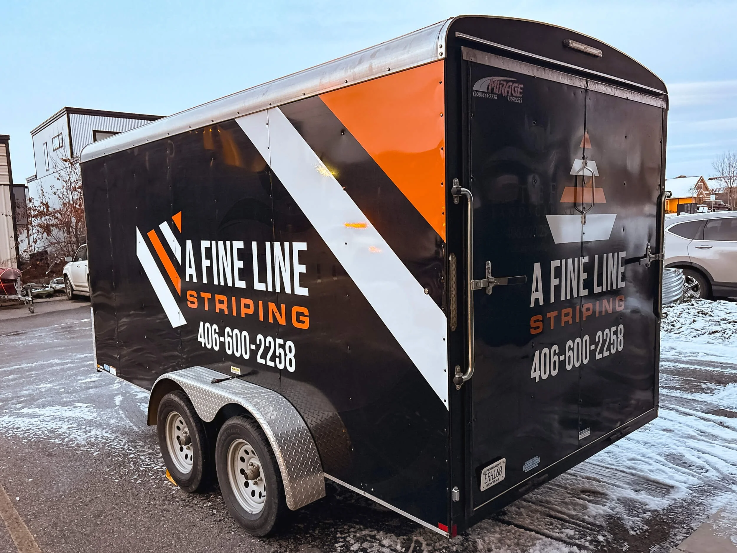 Angled view of the driver side and back of a small trailer with bright orange and white vinyl graphics adevertising for A Fine Line Striping