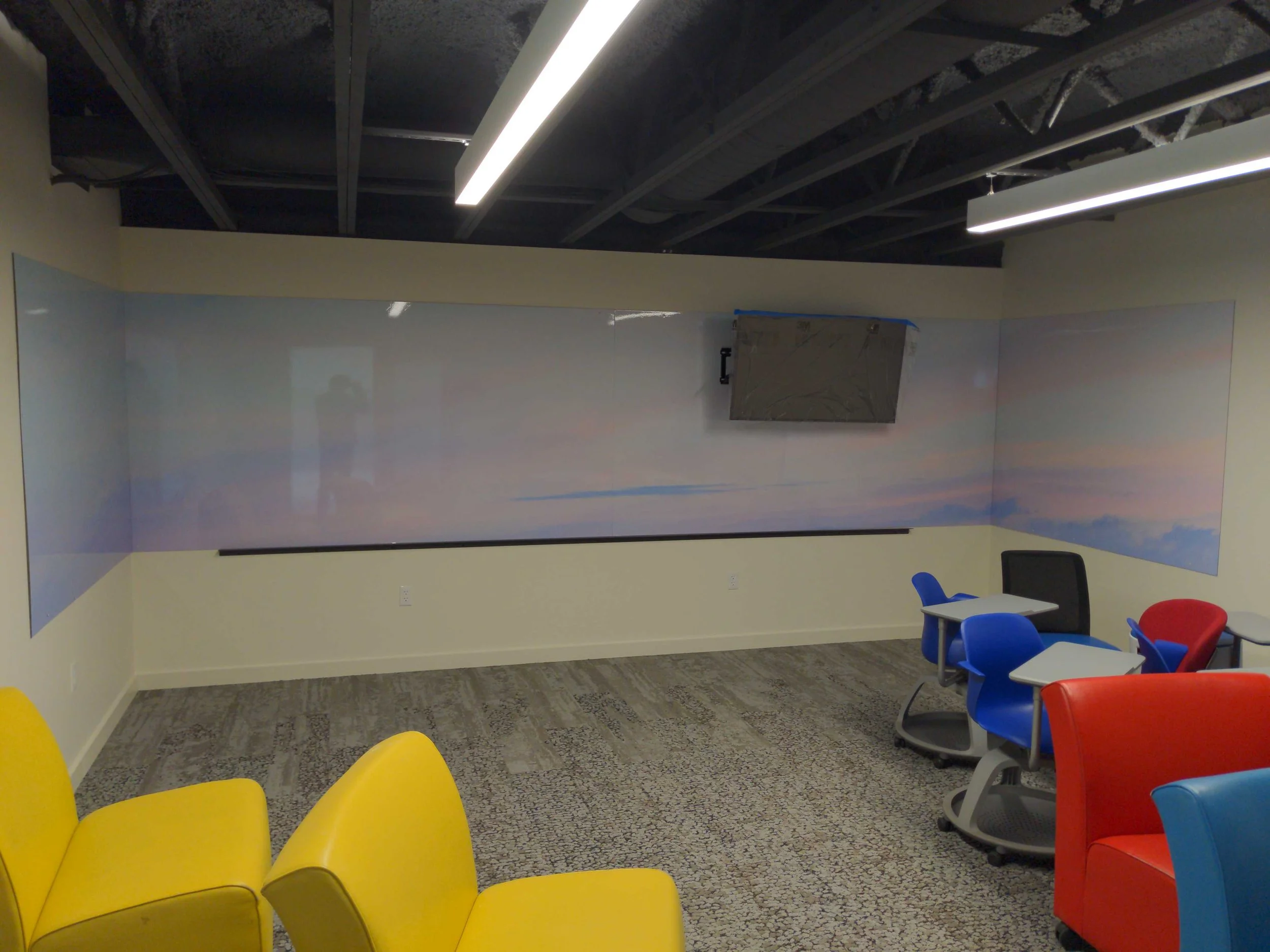 Pastel landscape wall wraps made from dry erase material in a room with colorful seating.