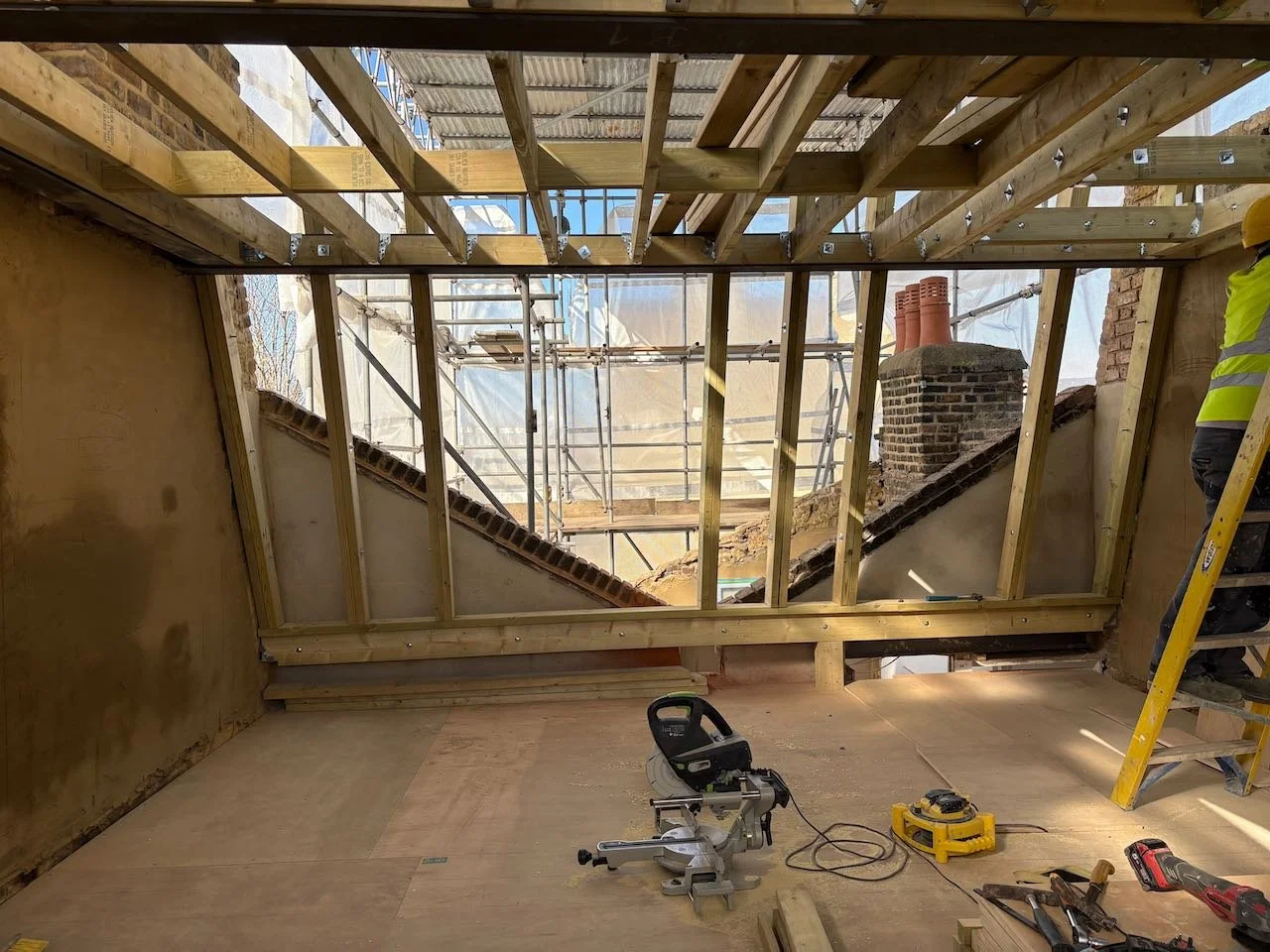 Construction-stage loft extension showing exposed timber structure and existing brickwork during a London home renovation