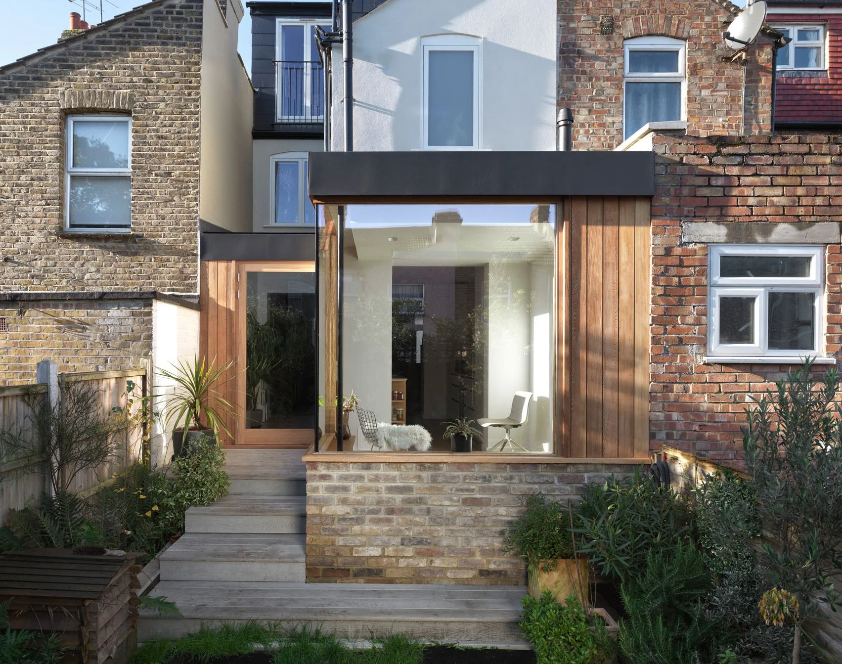 Rear view of a compact Victorian terrace extension with timber cladding, brick base and corner glazing