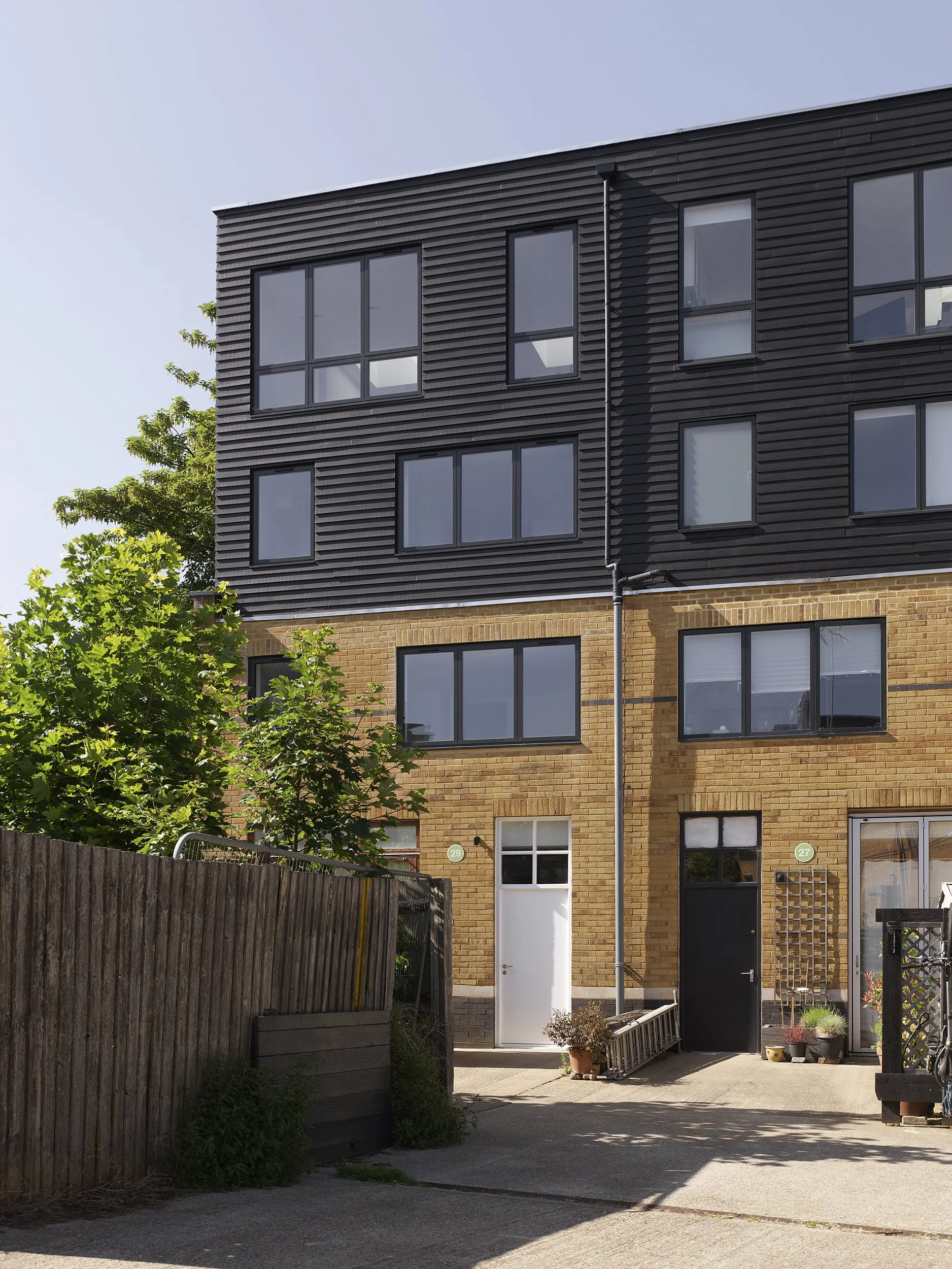 Two-storey roof extension added to mid-1990s live-work buildings in Hackney, with new upper floors set back above the original brick structure.