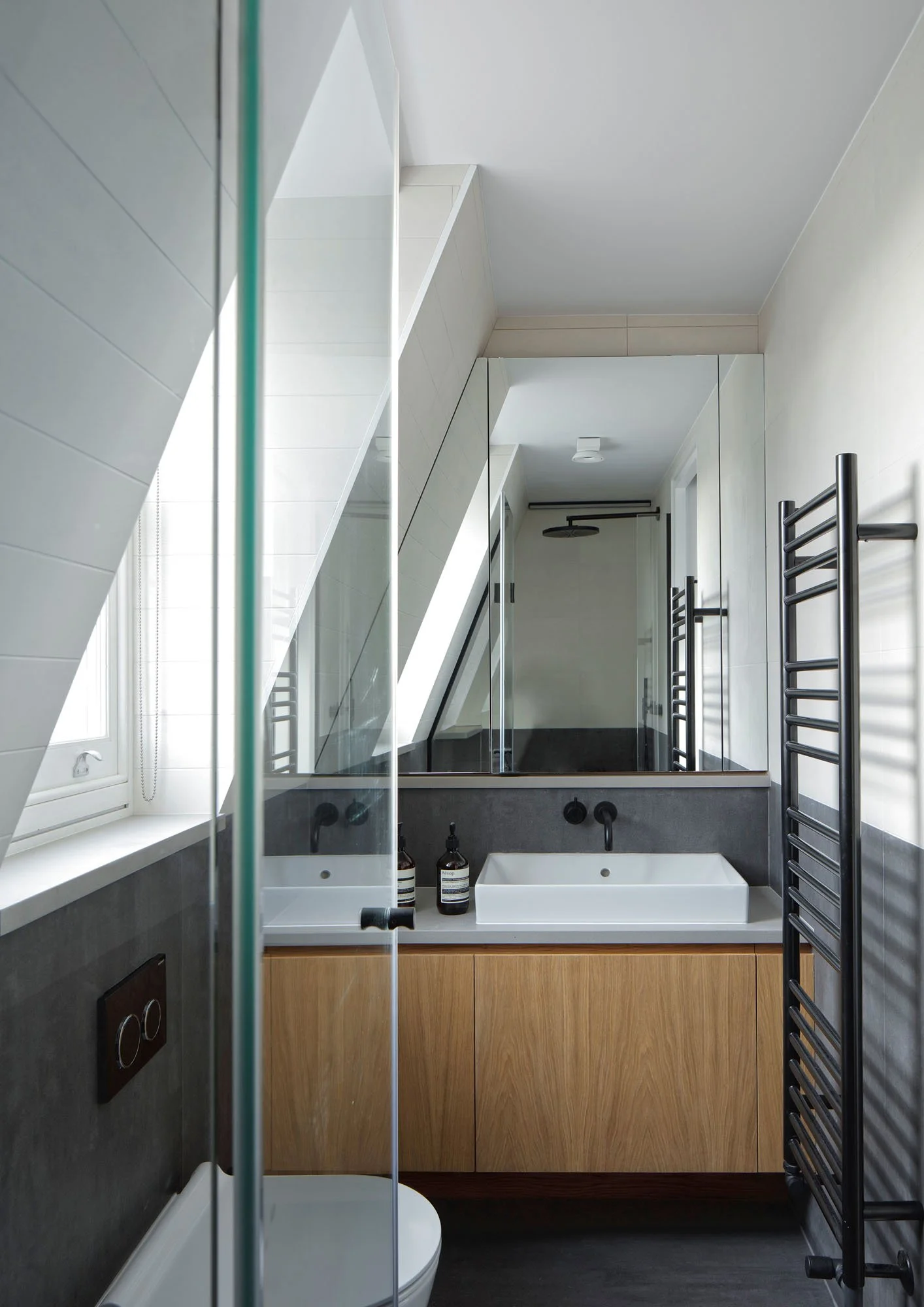 Compact ensuite bathroom at Prebend Street with rooflight, oak vanity and mirrored storage in an Islington loft extension.