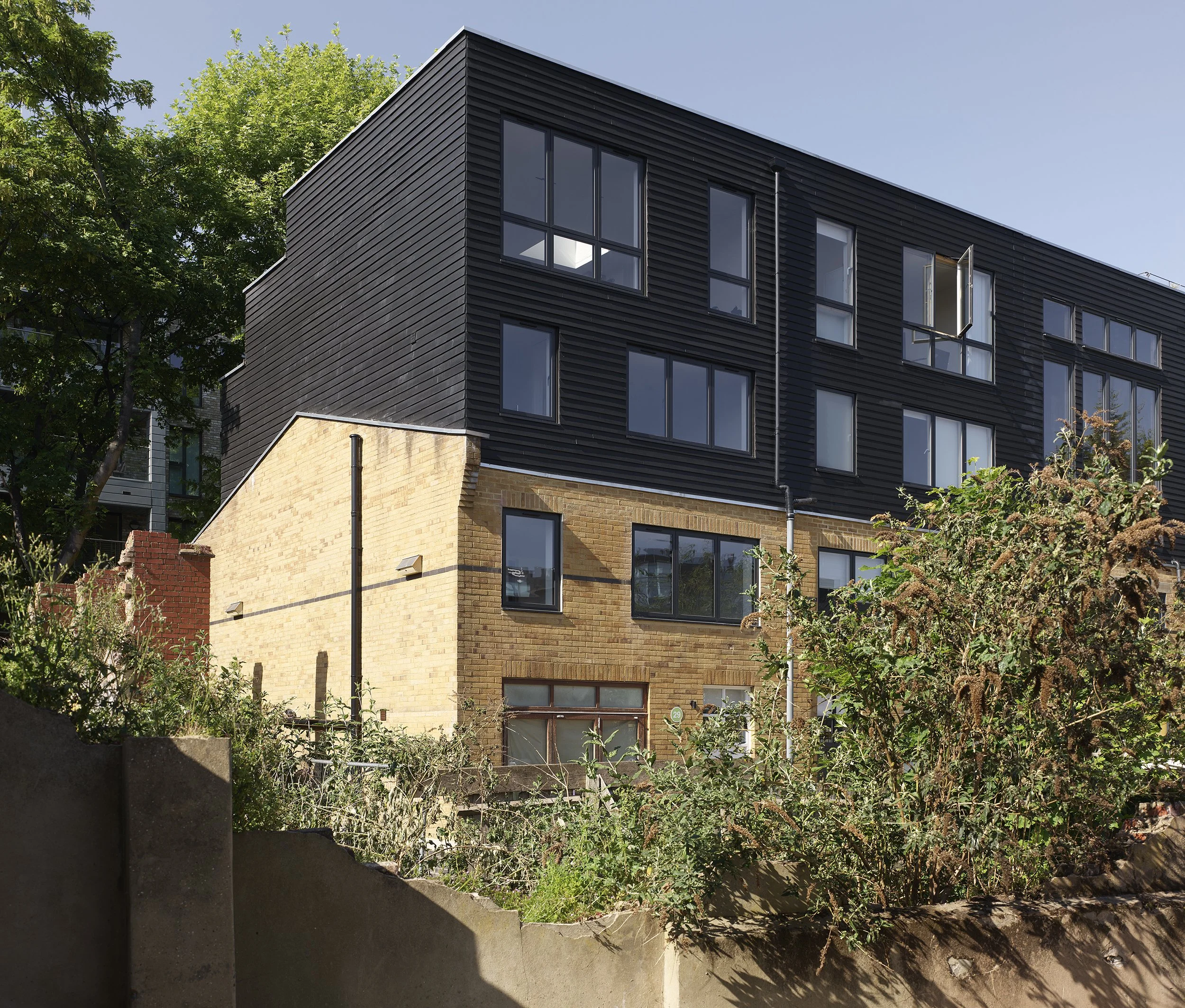 Two-storey roof extension added to mid-1990s live-work buildings in Hackney, with new upper floors set back above the original brick structure.