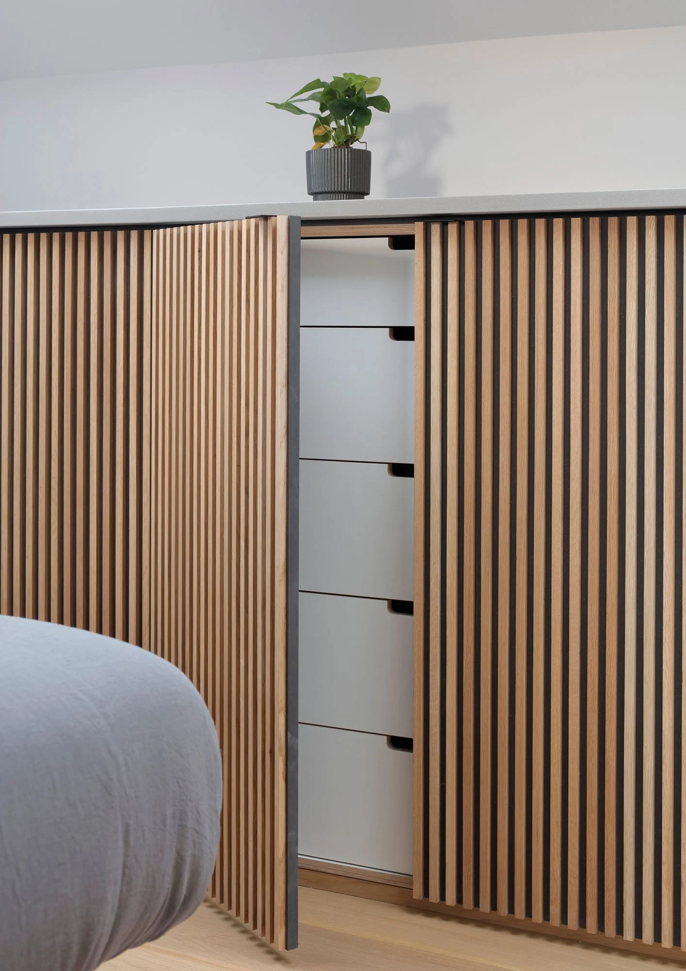 Bespoke slatted timber bedroom storage with concealed drawers in a London home renovation.