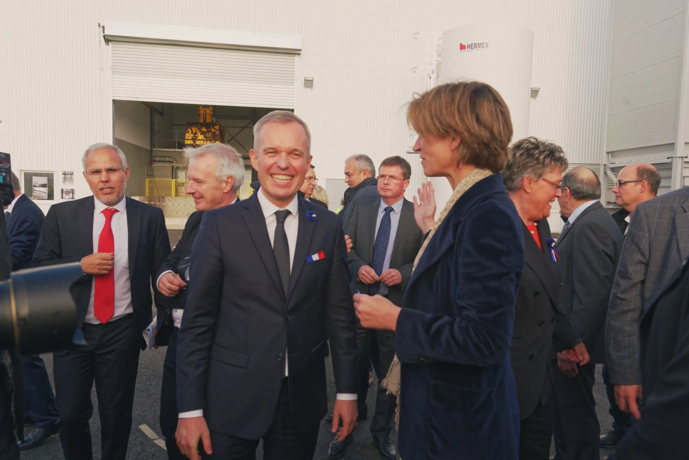 Photo of a politician smiling while having his picture taken, surrounded by many other people accompanying him.