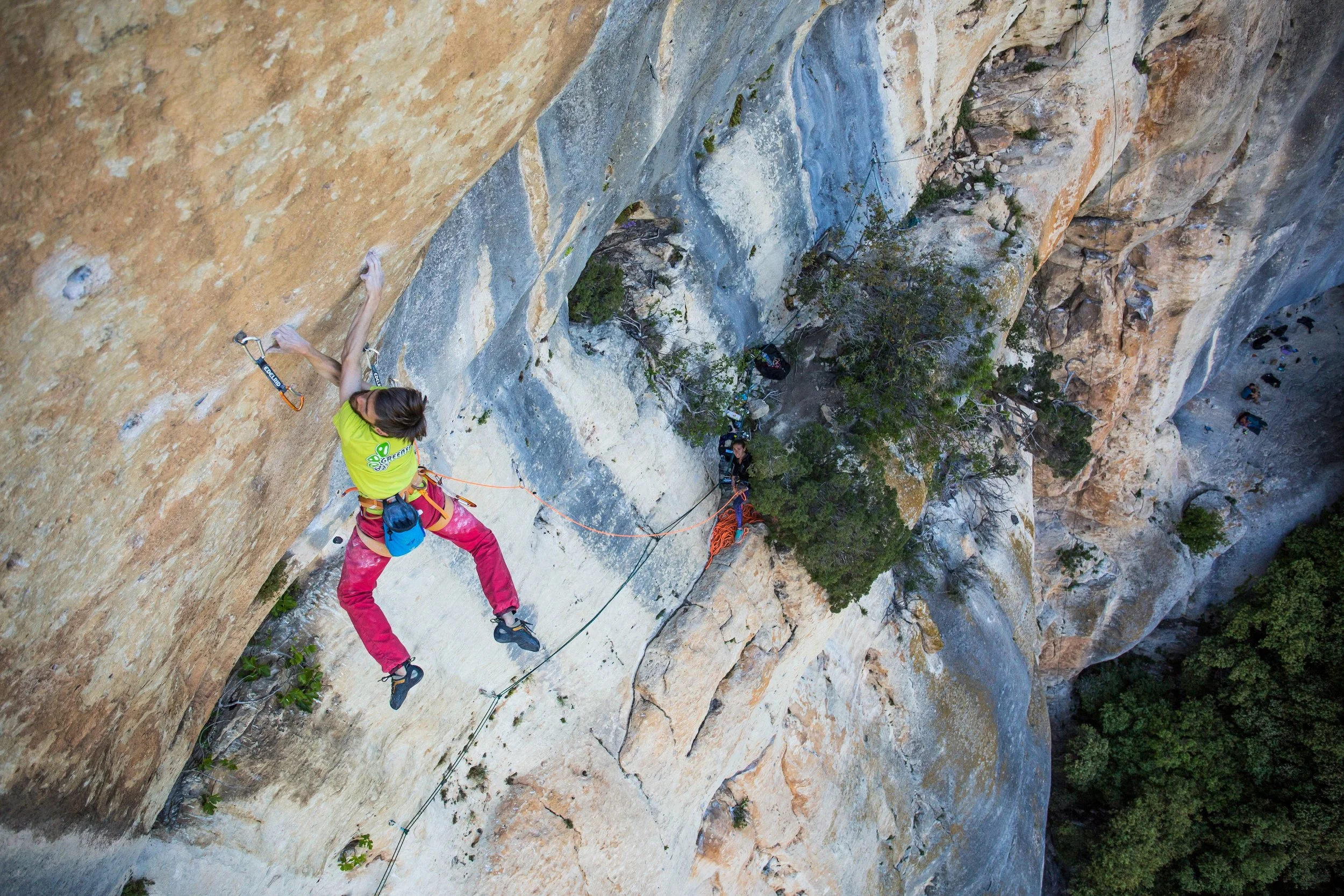 Une grimpeuse en falaise, équipée de harnais et corde, en train d'escalader une paroi rocheuse.