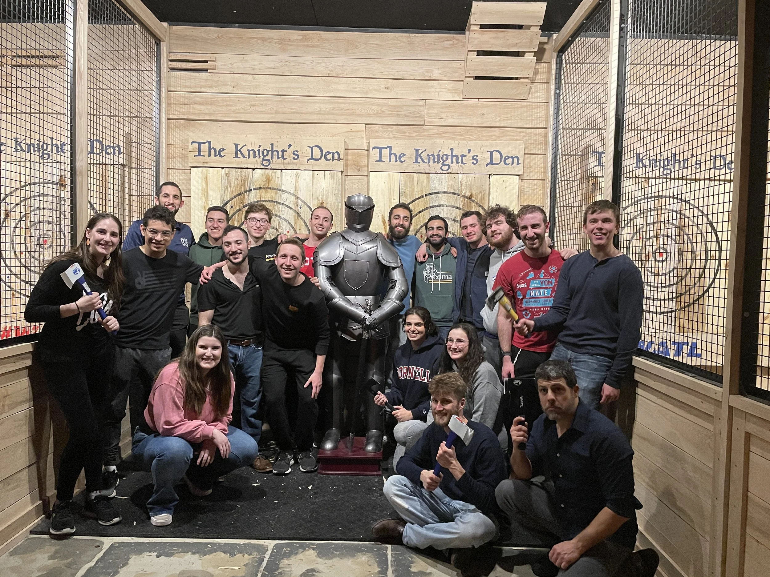 A group of people posing together inside a laser tag arena called The Knight's Den, with some holding axes and a person dressed in armor at the center.