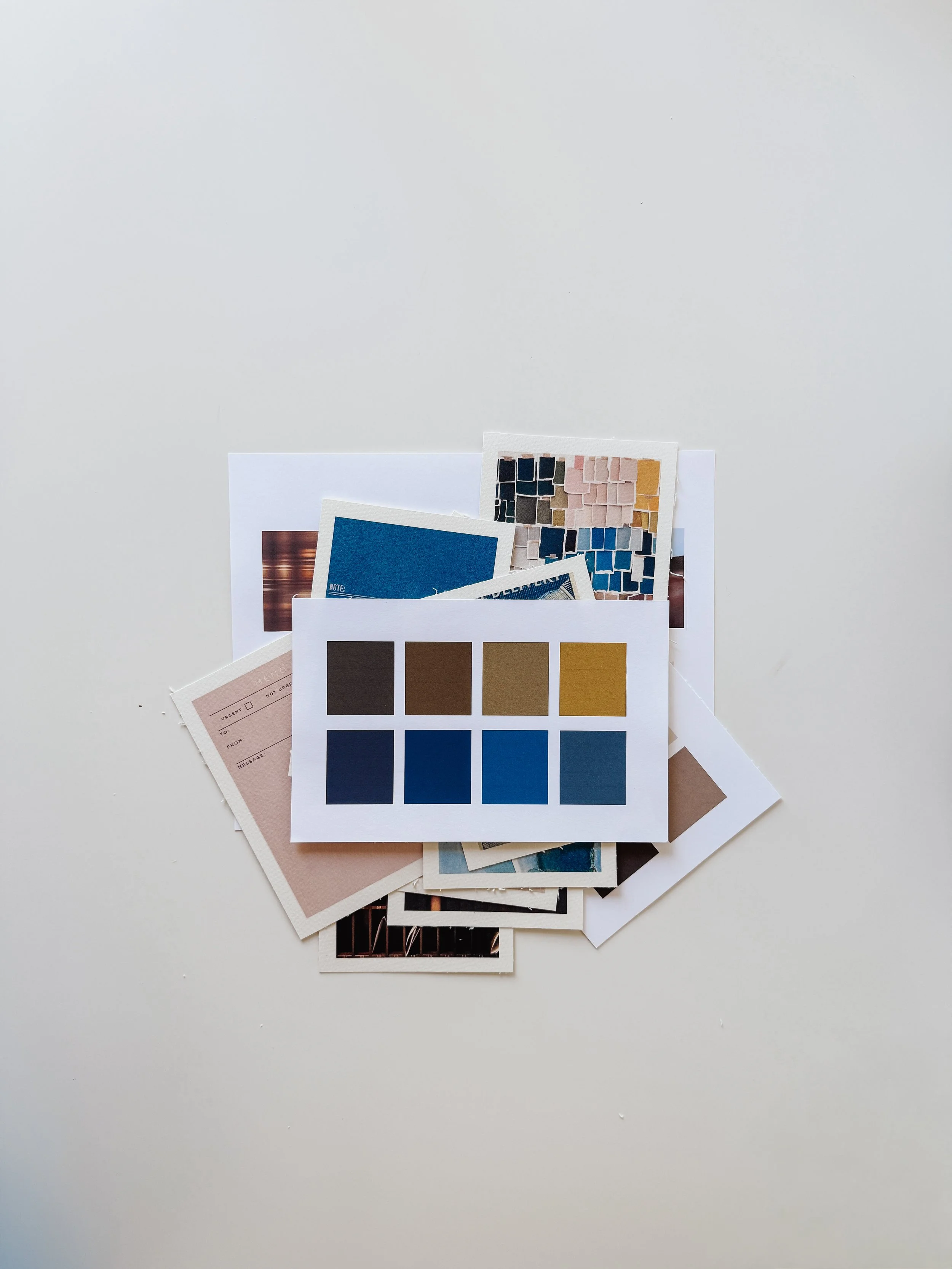 Various color swatches and sample cards scattered on a white surface, including a palette with different shades of blue, brown, and yellow, and some printed materials.