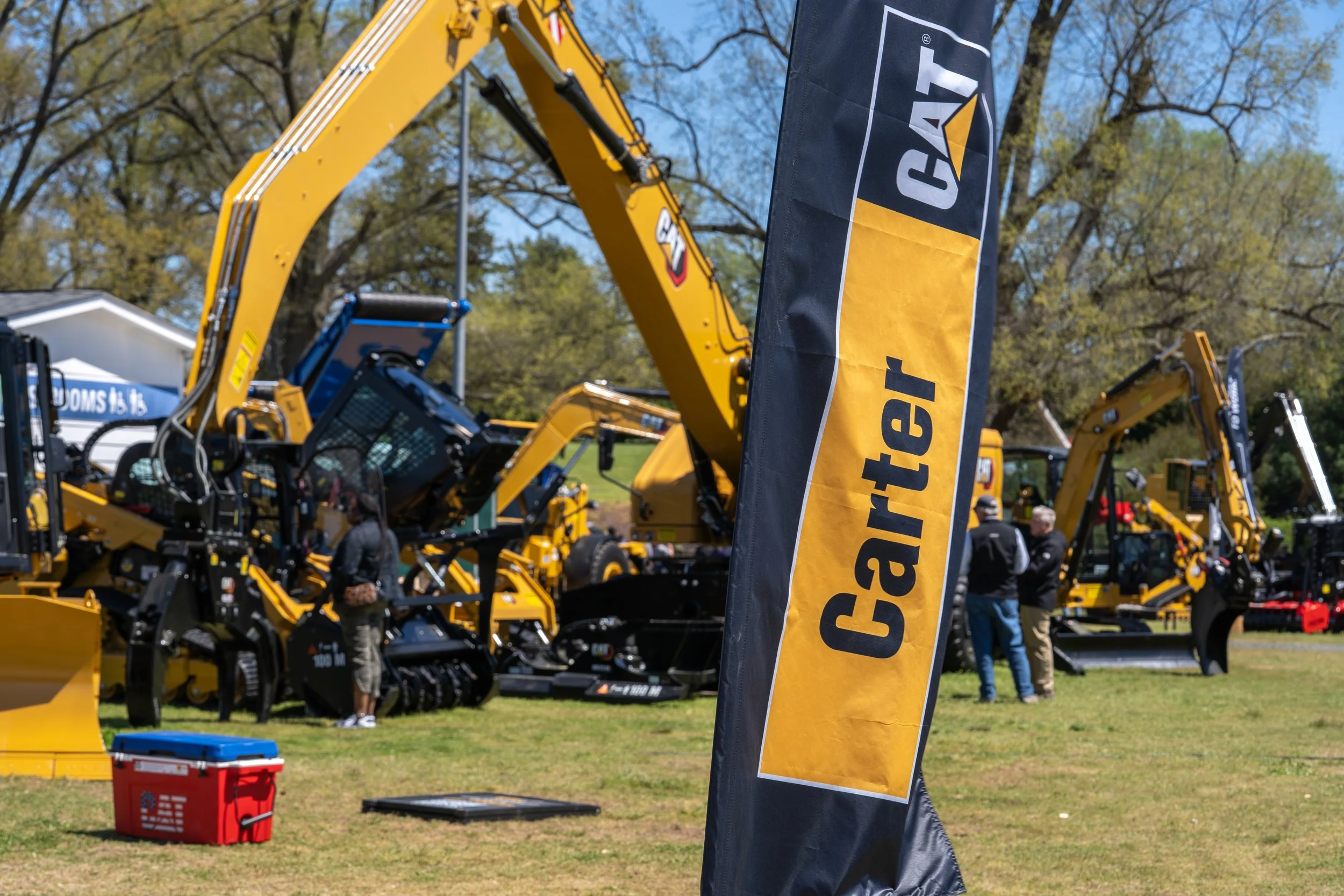 Construction equipment and machinery on display at an outdoor event, with a Caterpillar (CAT) flag prominently in the foreground.