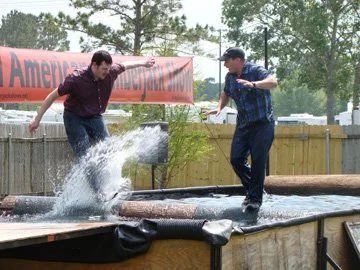 Two young men jumping into a water-filled trampoline, splashing water as they leap.