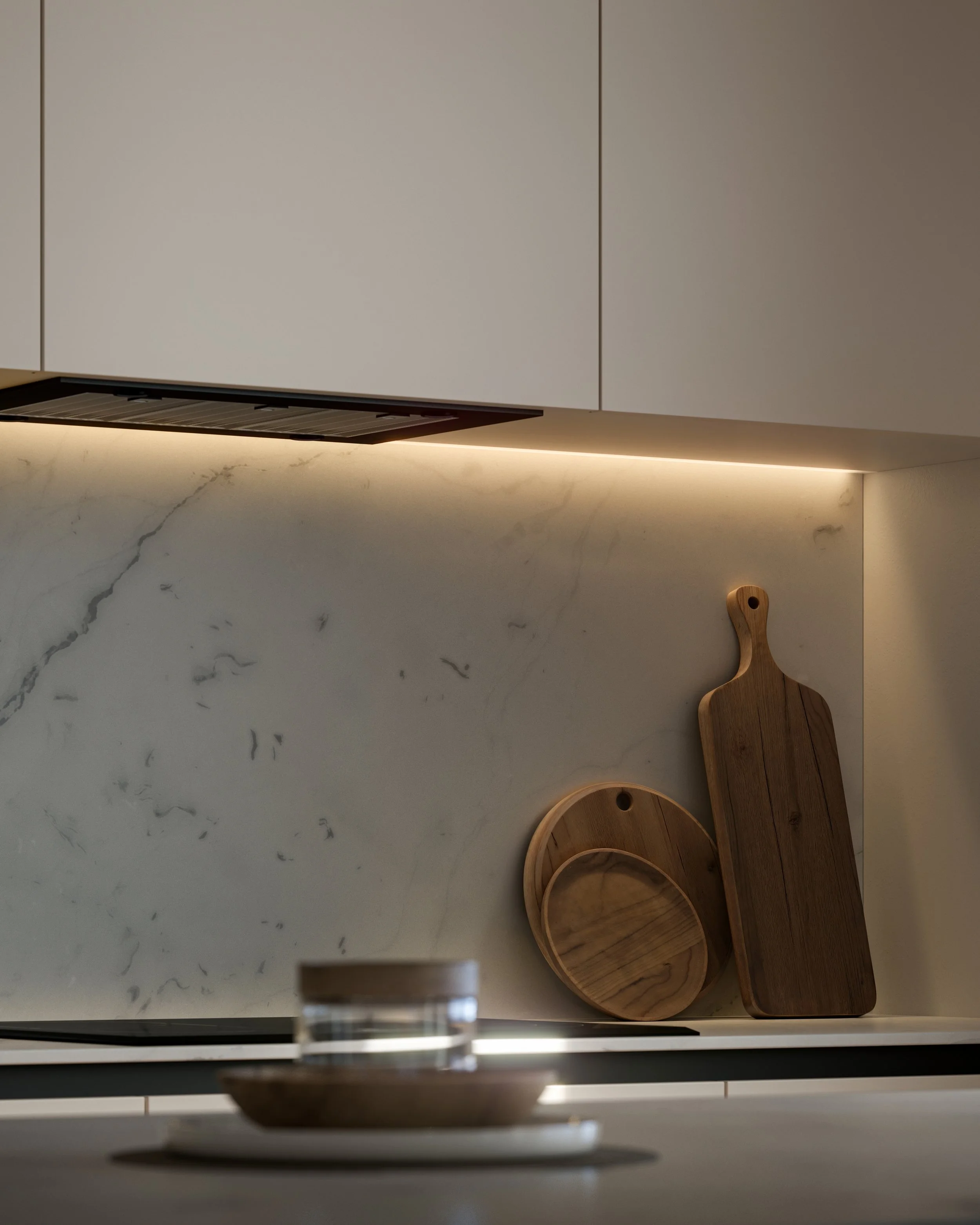 Close-up of a modern kitchen counter with wooden cutting boards and dishes, illuminated by under-cabinet lighting.