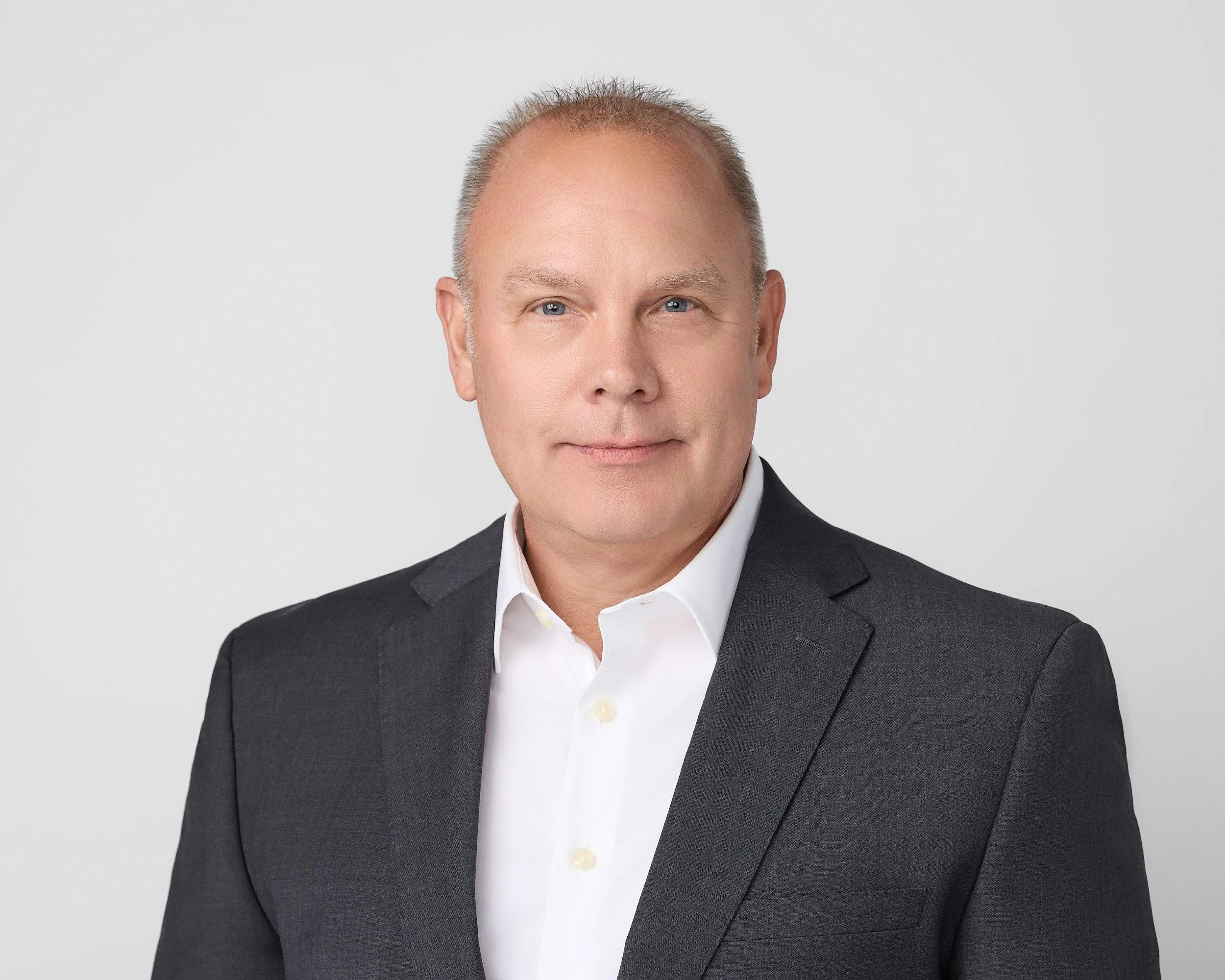 Professional headshot of a man in a gray suit and white shirt against a plain background.