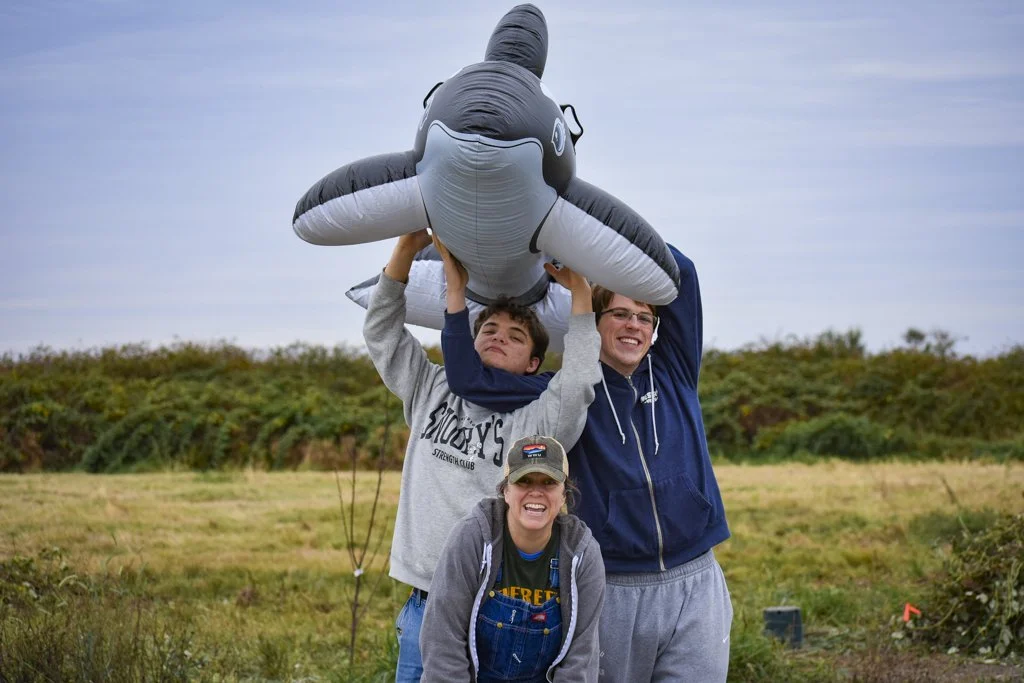 A woman and two teen boys smile while holding an inflatable orca
