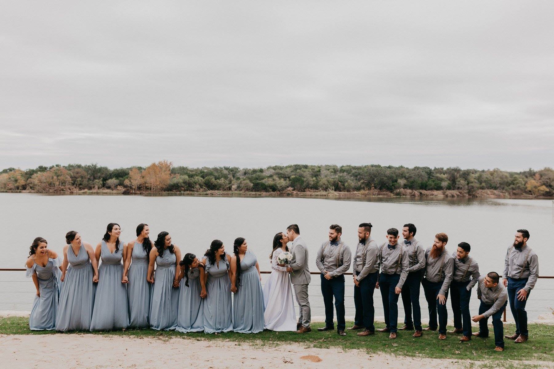 Lake backdrop with large wedding party, couple is kissing