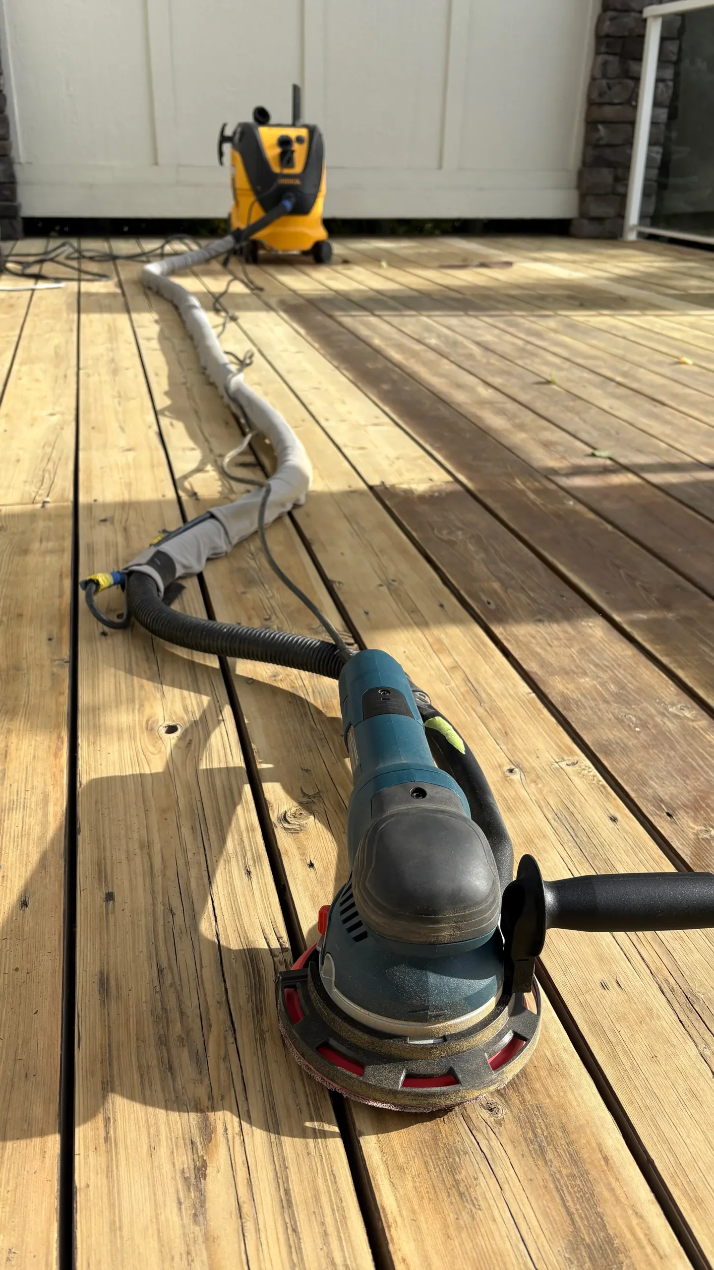 A power sander on a wooden deck, with a yellow pressure washer in the background.