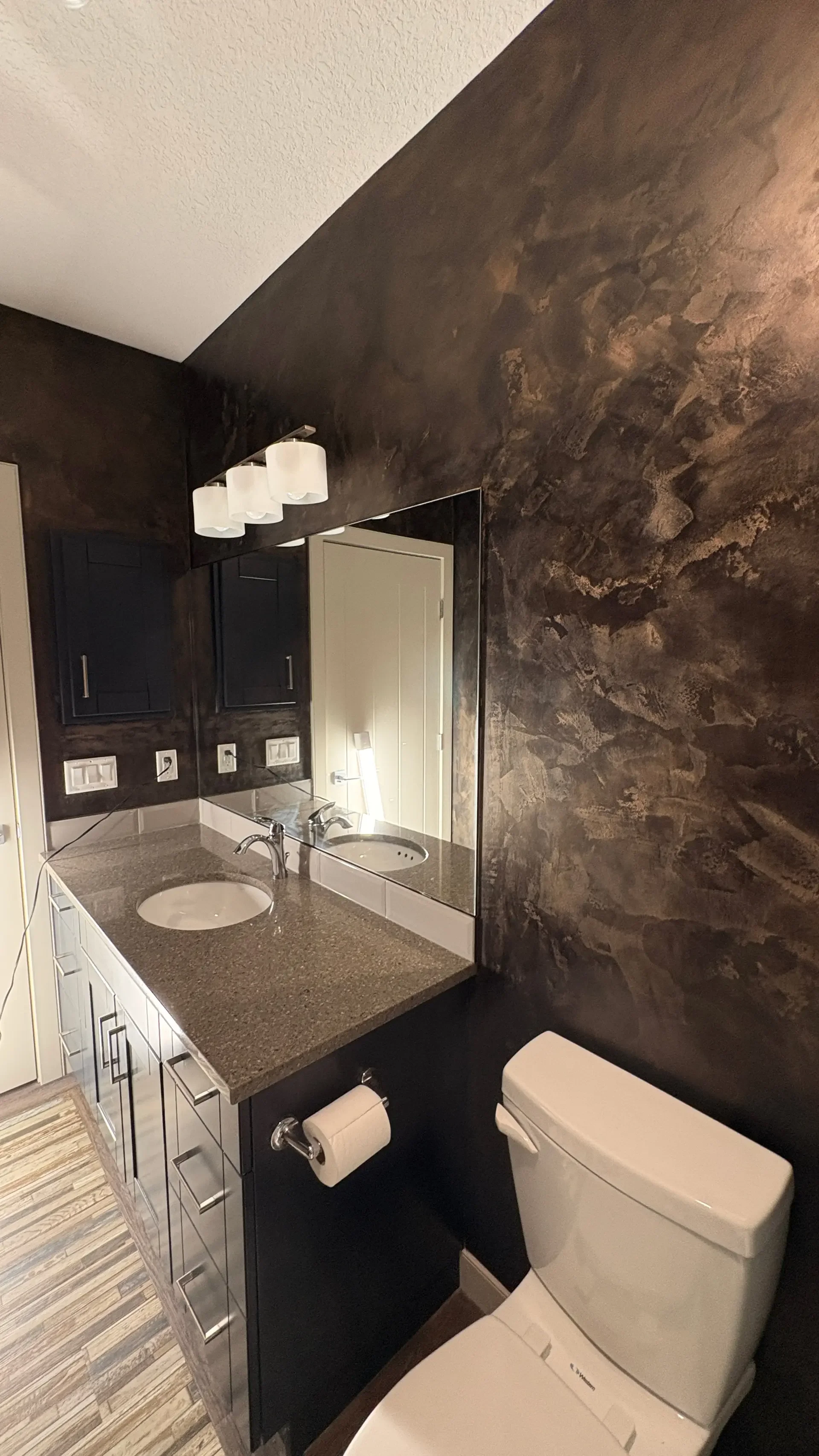 Bathroom with dark and light cabinets, granite countertop, large mirror, white toilet, and wall-mounted light fixture.