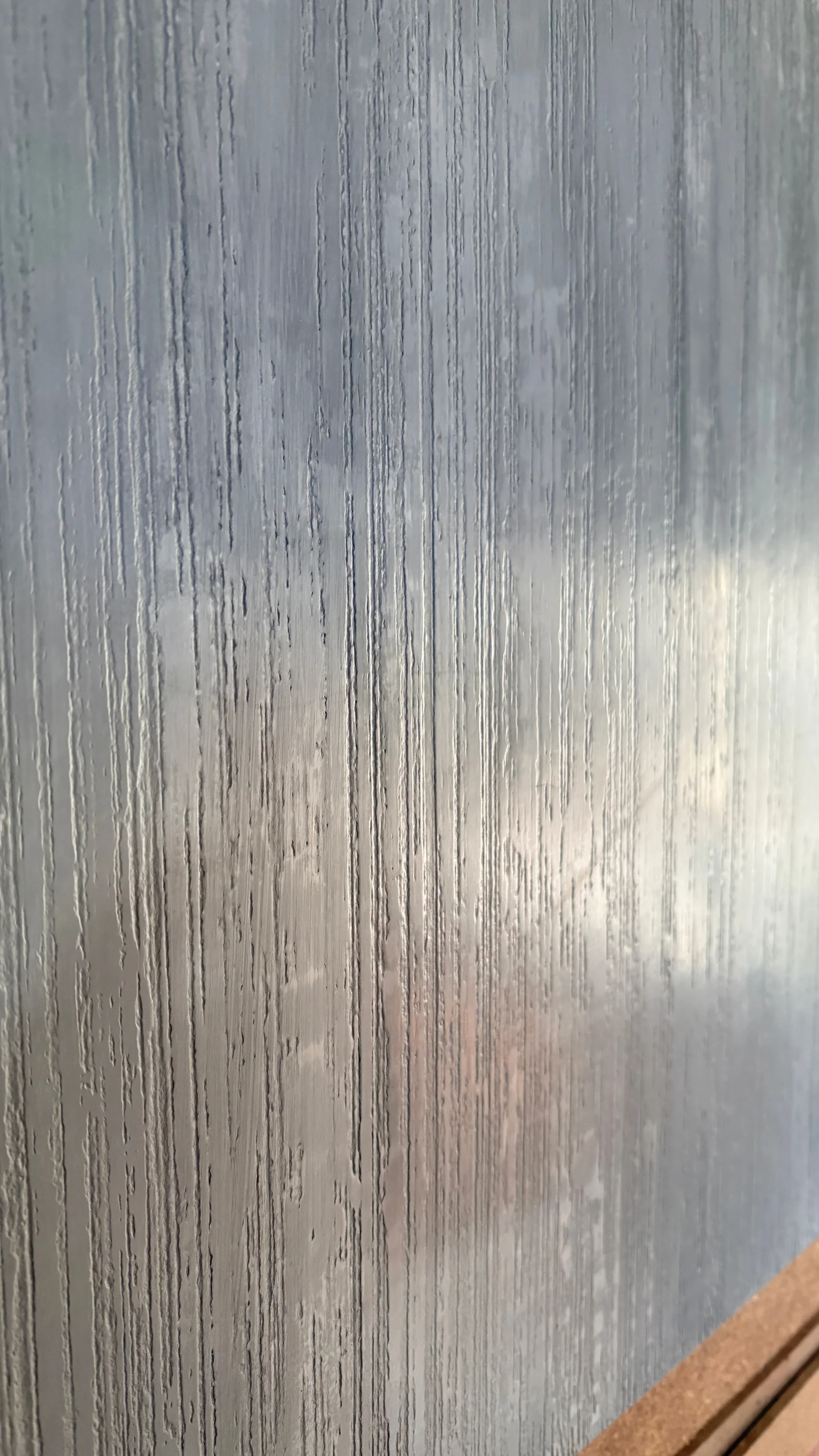 Close-up of a frosted glass window with water droplets and streaks.