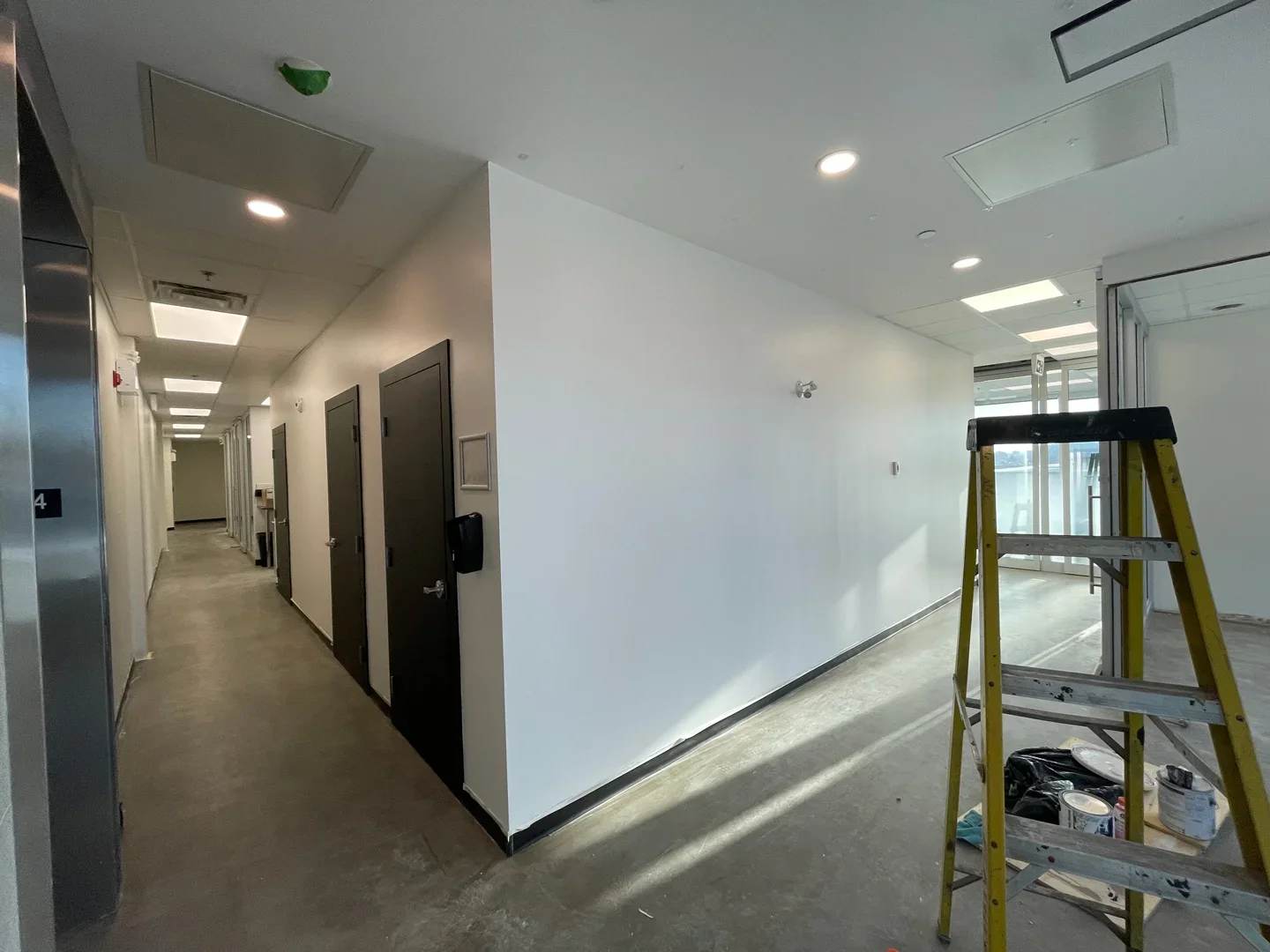 Interior of a commercial or office building hallway with black doors, a ladder, and construction supplies.
