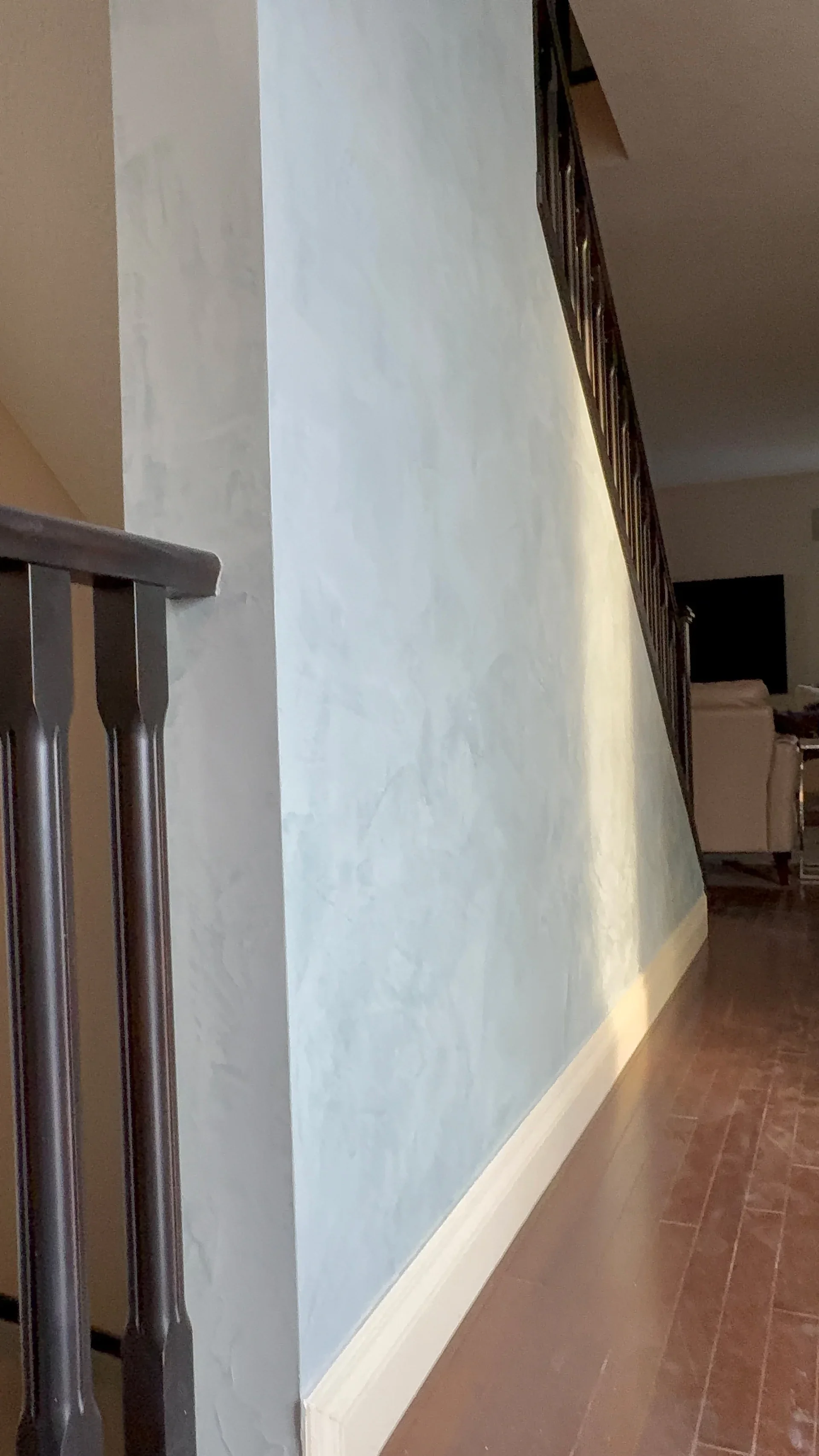 Interior view of a home with a blue textured wall, dark wood handrail, and a staircase.