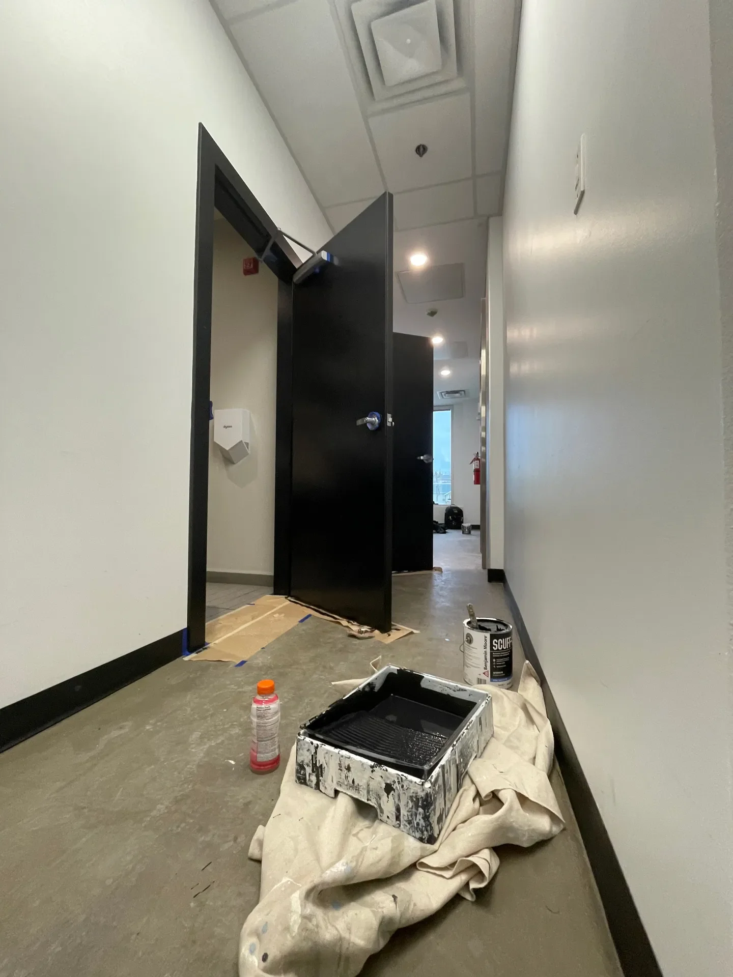 Hallway with black doors, a paint tray with black paint on a blanket, a small bottle, and a paint can, suggesting ongoing painting work.