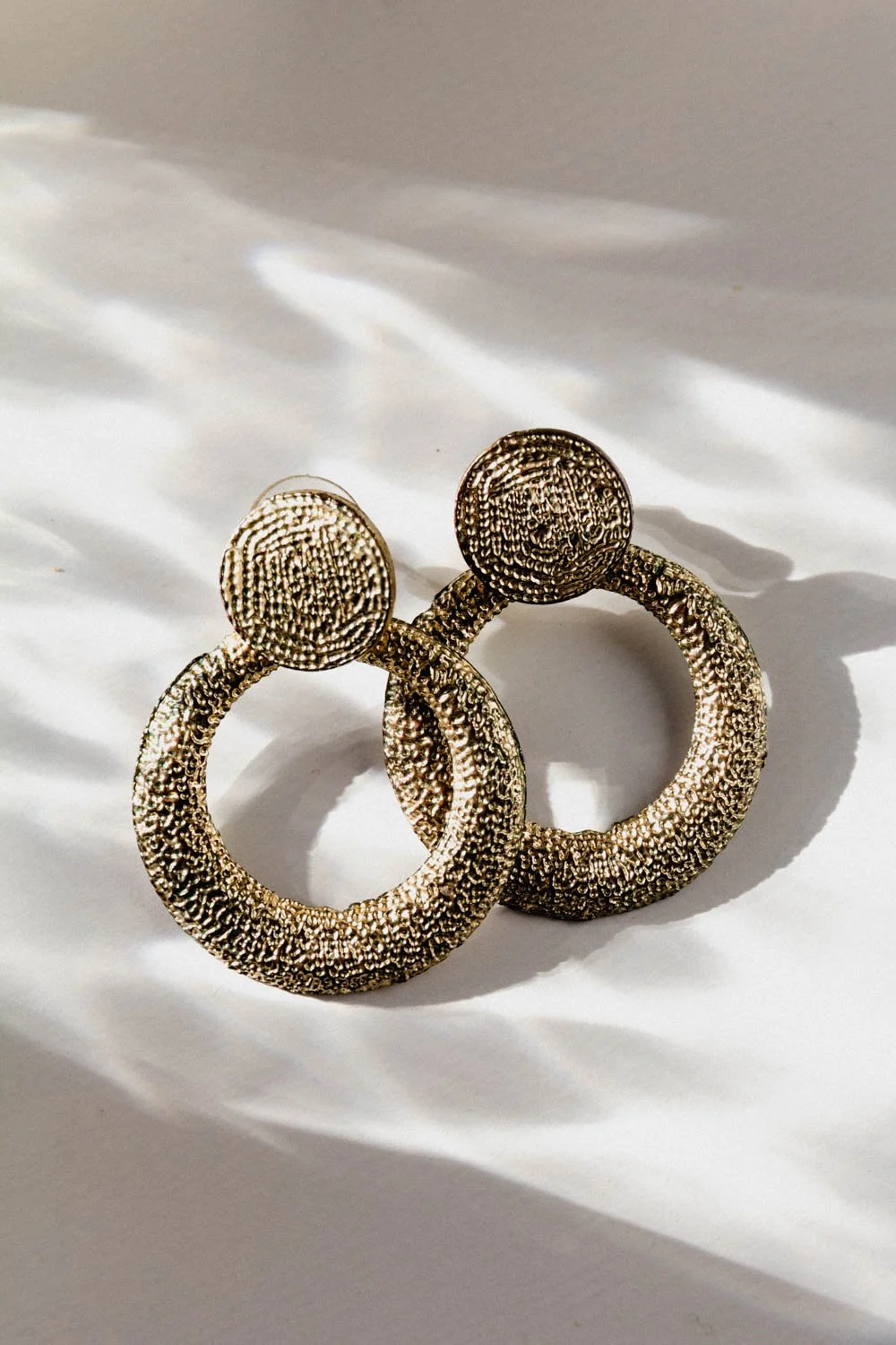 Pair of textured gold rings with round top and open circular band, placed on white surface with shadows