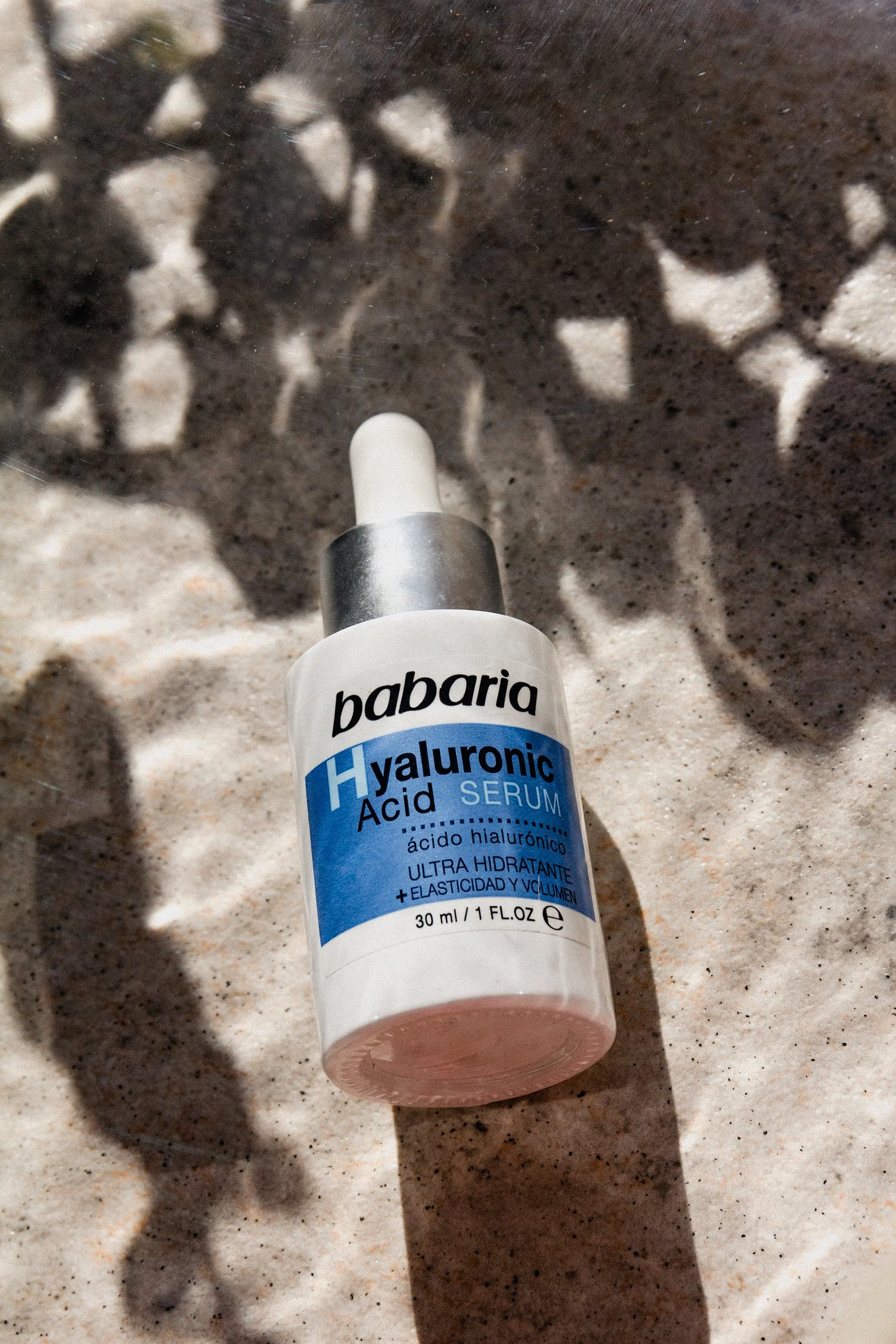 a bottle of liquid babaria on a sandy background with water and leaf shadow effects 