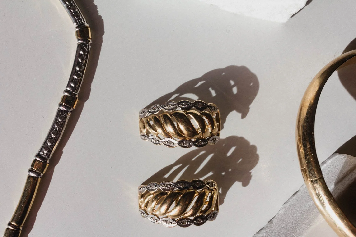 close up gold bracelet, earrings and pendant set on marble pieces and white background 