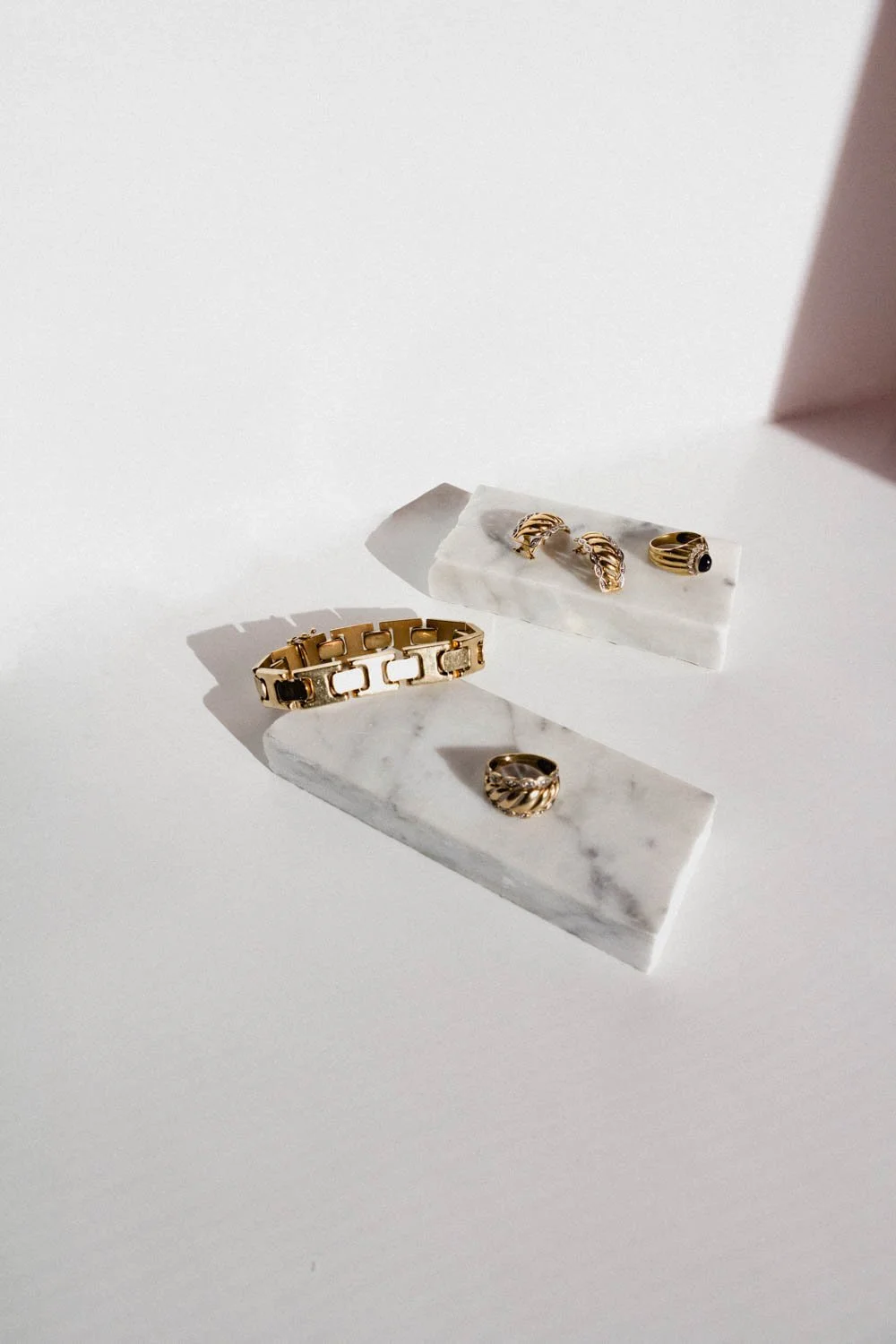 gold bracelet, earrings and rings on marble pieces on a white background
