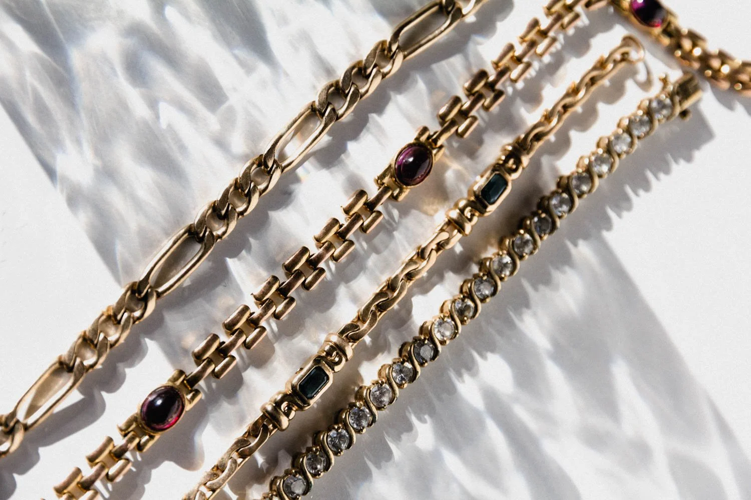 four gold bracelets with gemstones on a white background