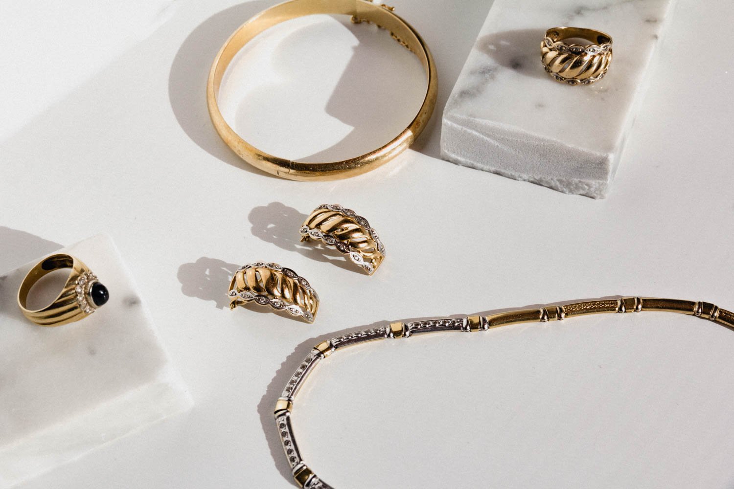 set of gold ring, bracelet, earrings and necklace on marble pieces and white background 
