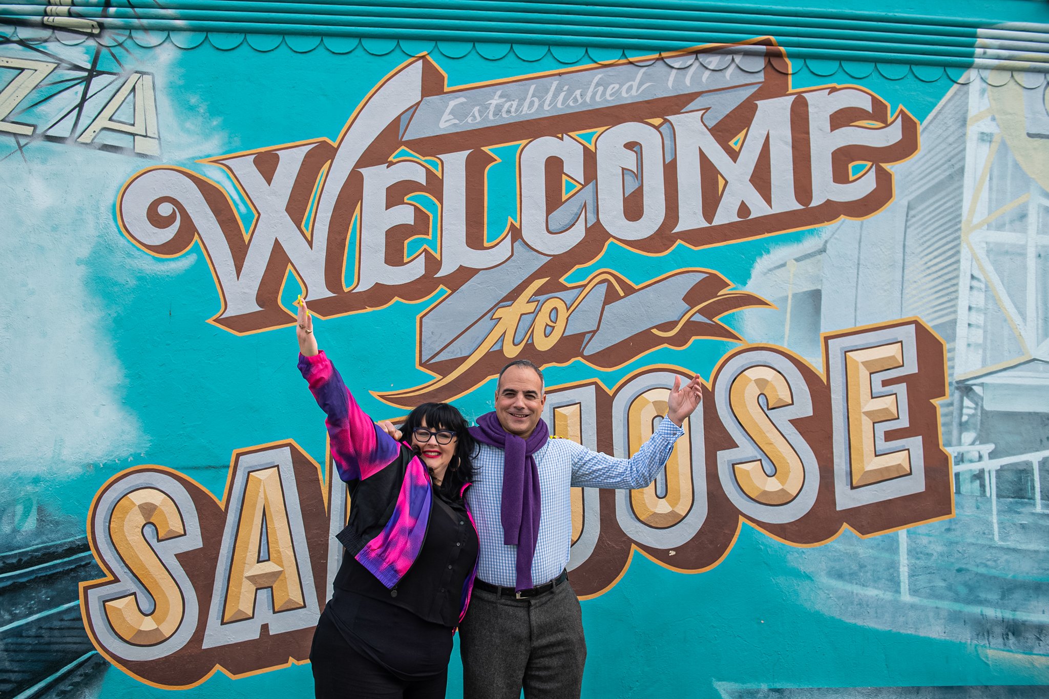Maestro Joseph Marcheso and General Director Shawna Lucey of Opera San Jose stand in front of a Welcome to San Jose mural