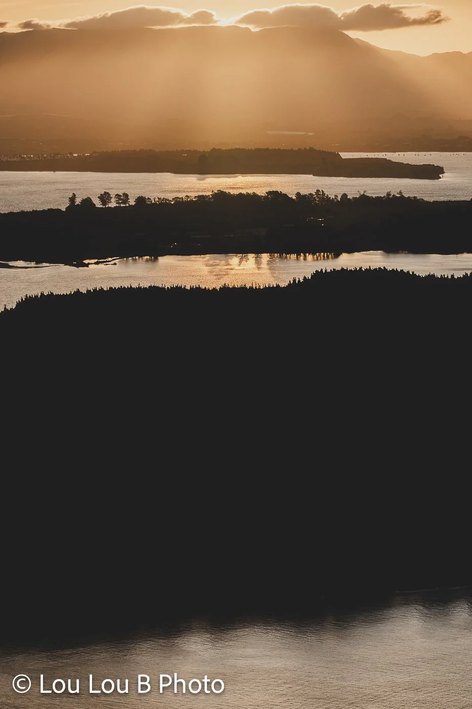 Layered coastal landscape silhouetted beneath warm golden sunlight and hazy mountains.