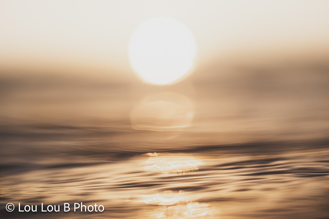 Dreamlike close-up of the sun reflecting across softly blurred golden ocean water.