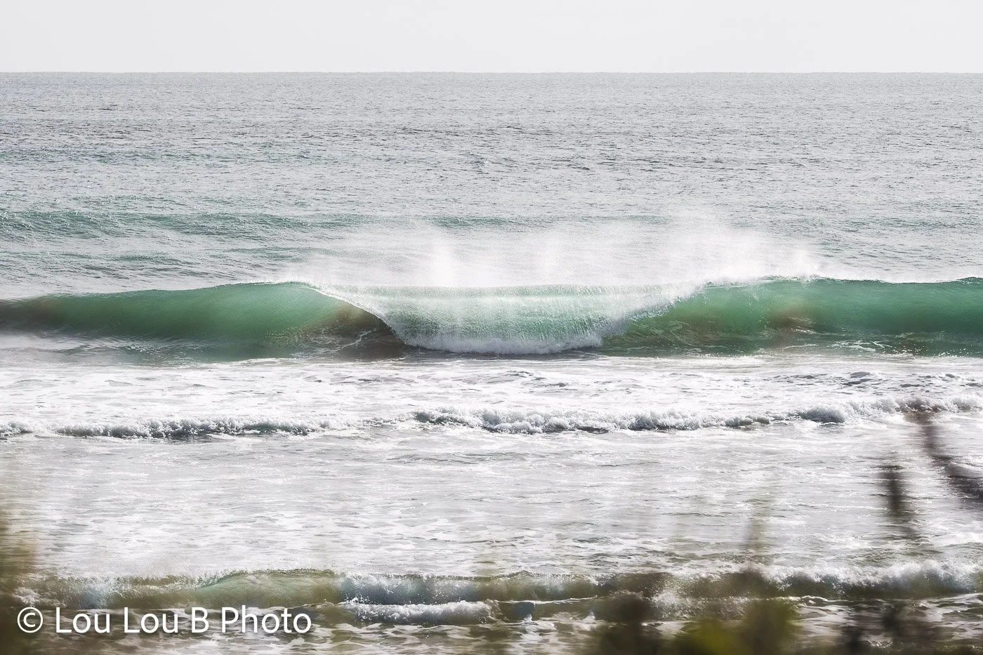 Green ocean wave breaking towards shore with offshore spray.