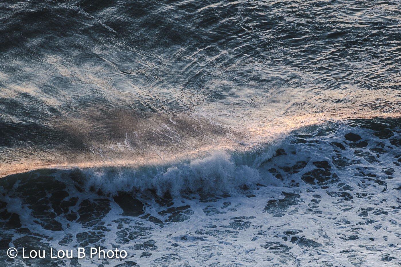 Powerful ocean wave breaking with offshore spray illuminated by warm morning light.