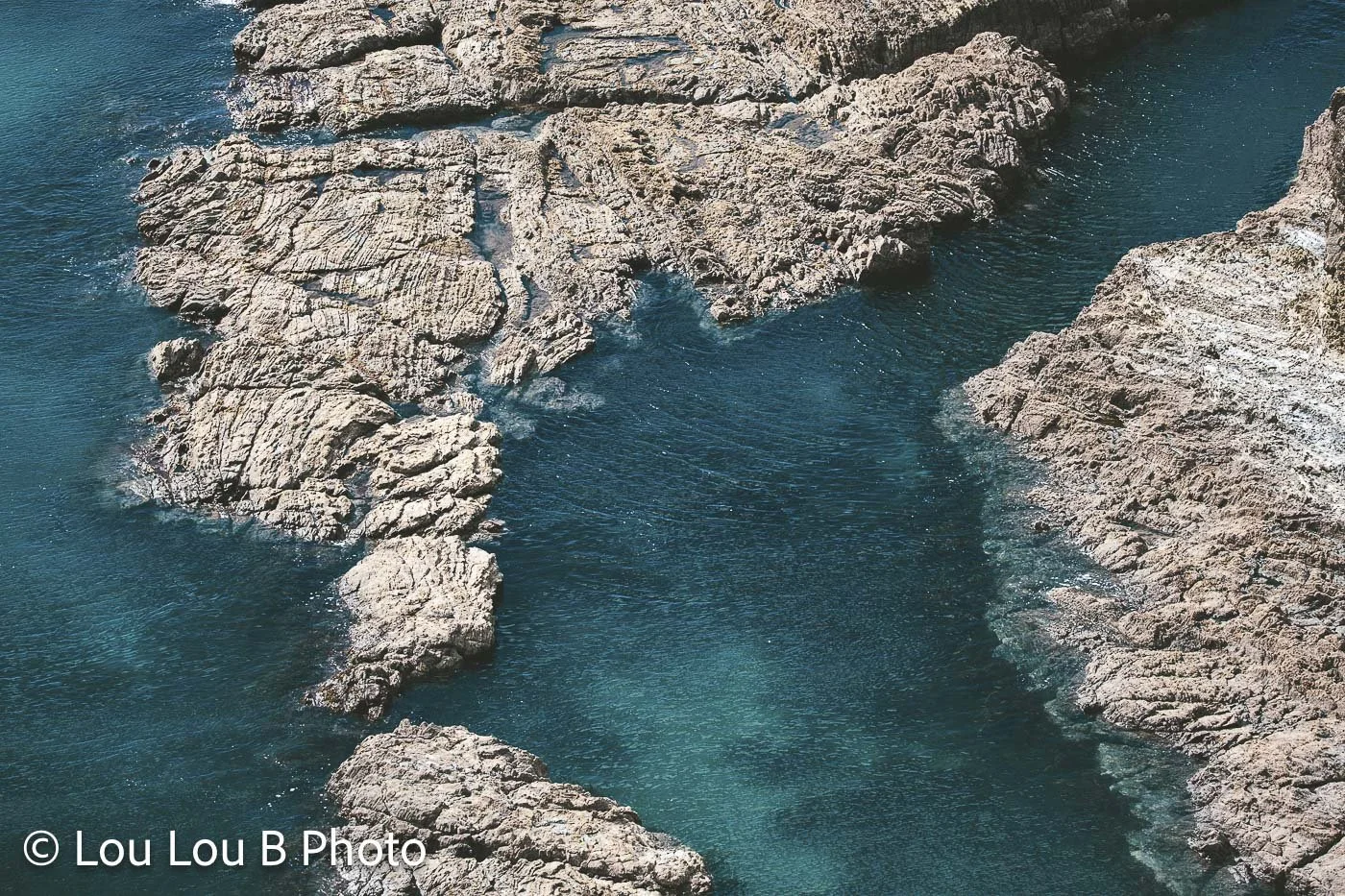 Rocky coastline surrounded by clear deep turquoise Mediterranean water.