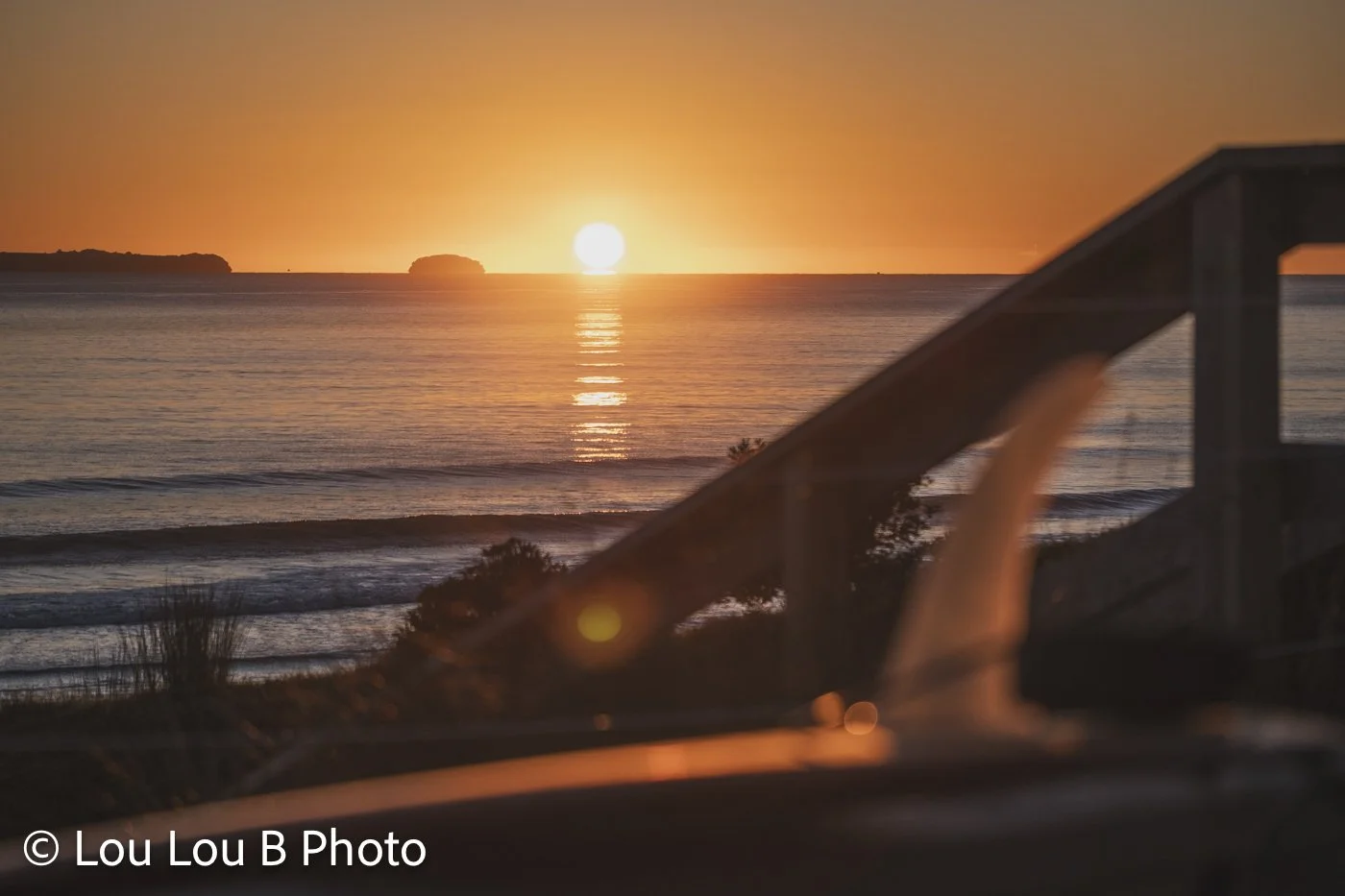 Sunrise over the ocean at Mount Maunganui with Motiti Island, with beach access and blurry longboard surfboard and fin in the foreground