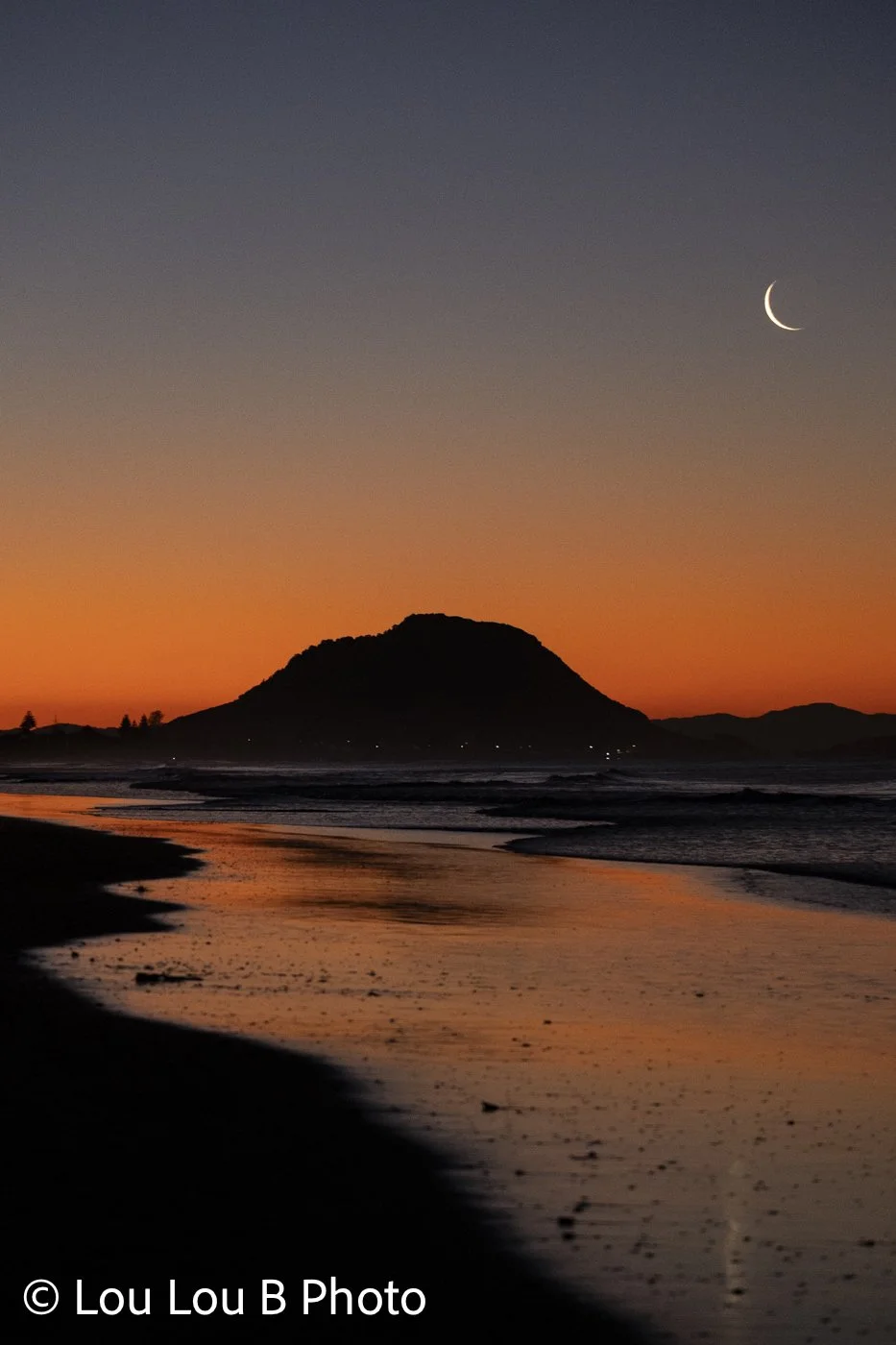 Crescent moon above Mauao and Mount Maunganui beach at orange twilight