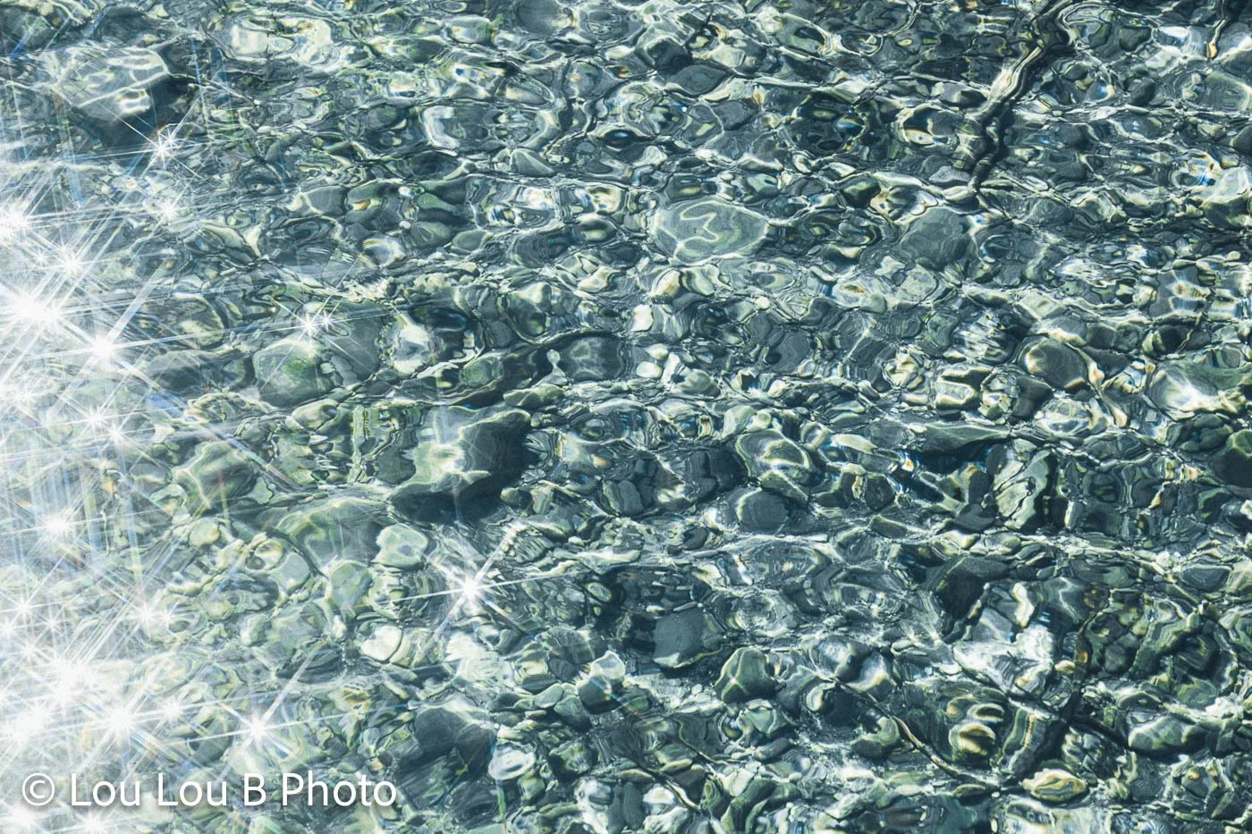 Sunlight sparkling across clear shallow turquoise water and underwater rocks.