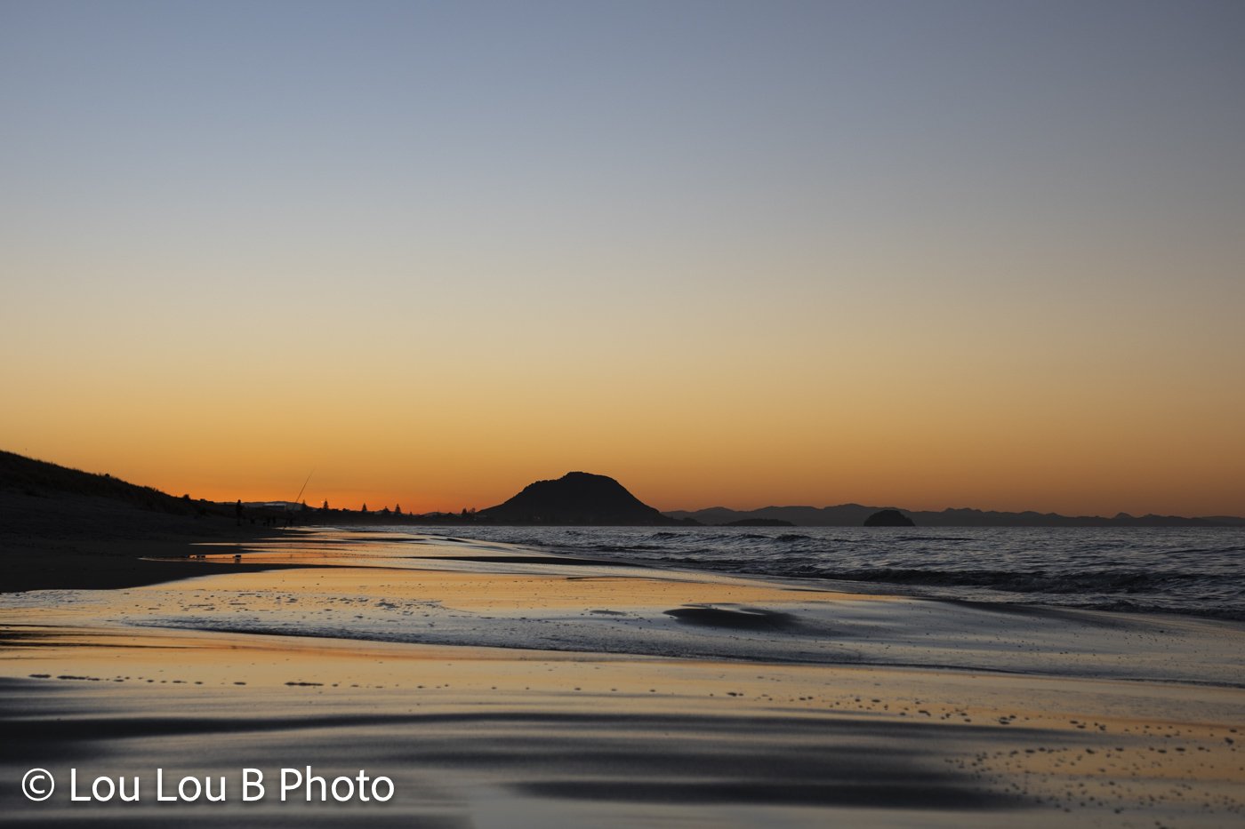 Mauao and Mount Maunganui beach at sunset with orange twilight reflected across wet sand