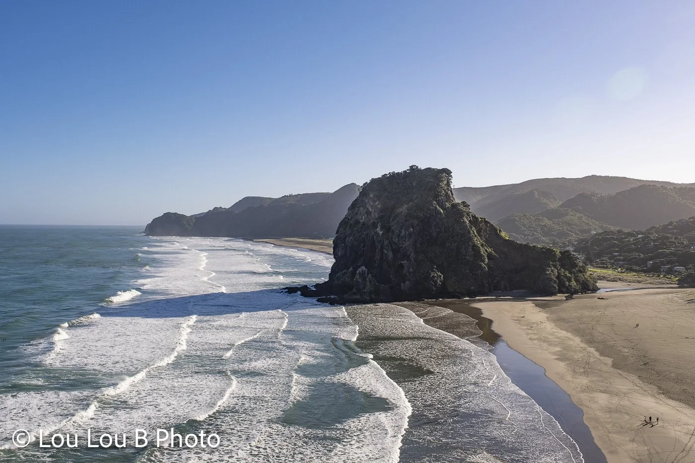 Wide coastal view of powerful waves breaking in parallel lines along a dramatic black-sand beach.