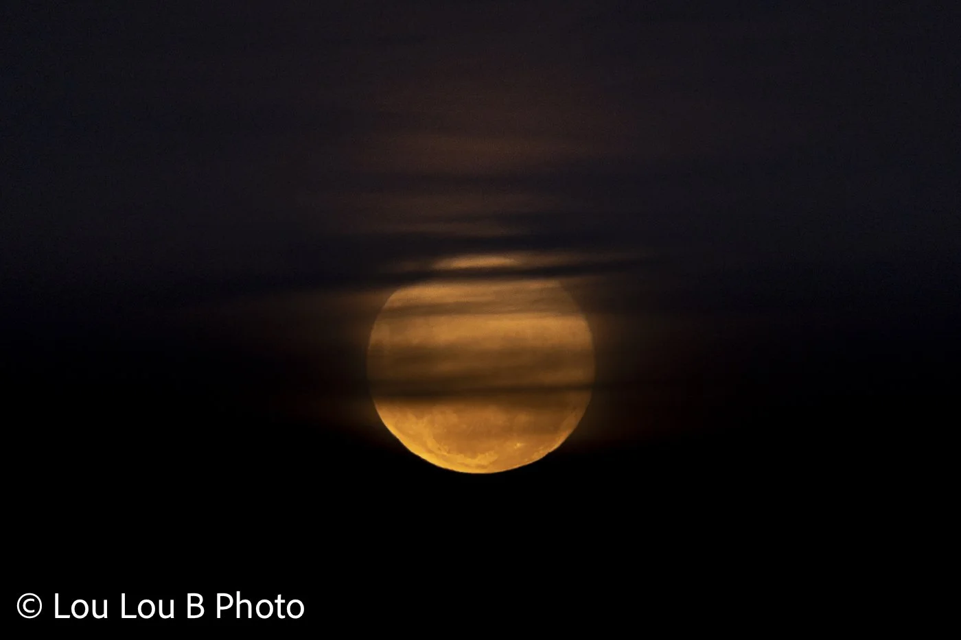 Golden moon partially obscured by dark atmospheric clouds.