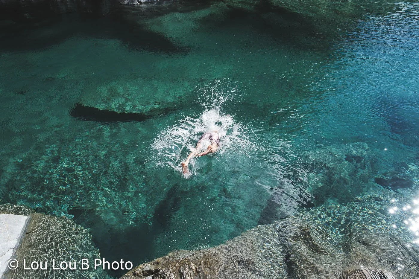 Swimmer in clear turquoise water beside a rocky coastal swimming platform.