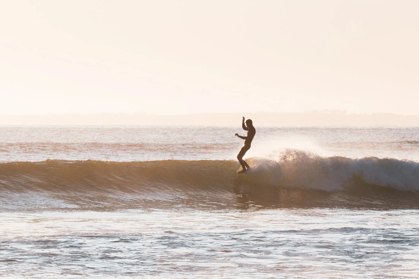 surfer riding wave photographed from beach at mid-range telephoto focal length around 164mm
