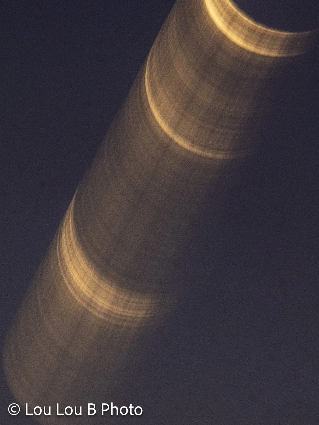 Abstract multiple-exposure photograph of a crescent moon creating a sweeping golden trail through a dark sky.