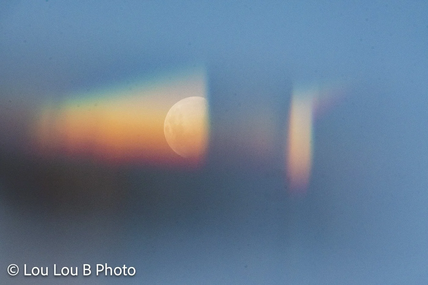 Abstract moon photography with a glowing moon distorted through rainbow-coloured light and soft blue tones.