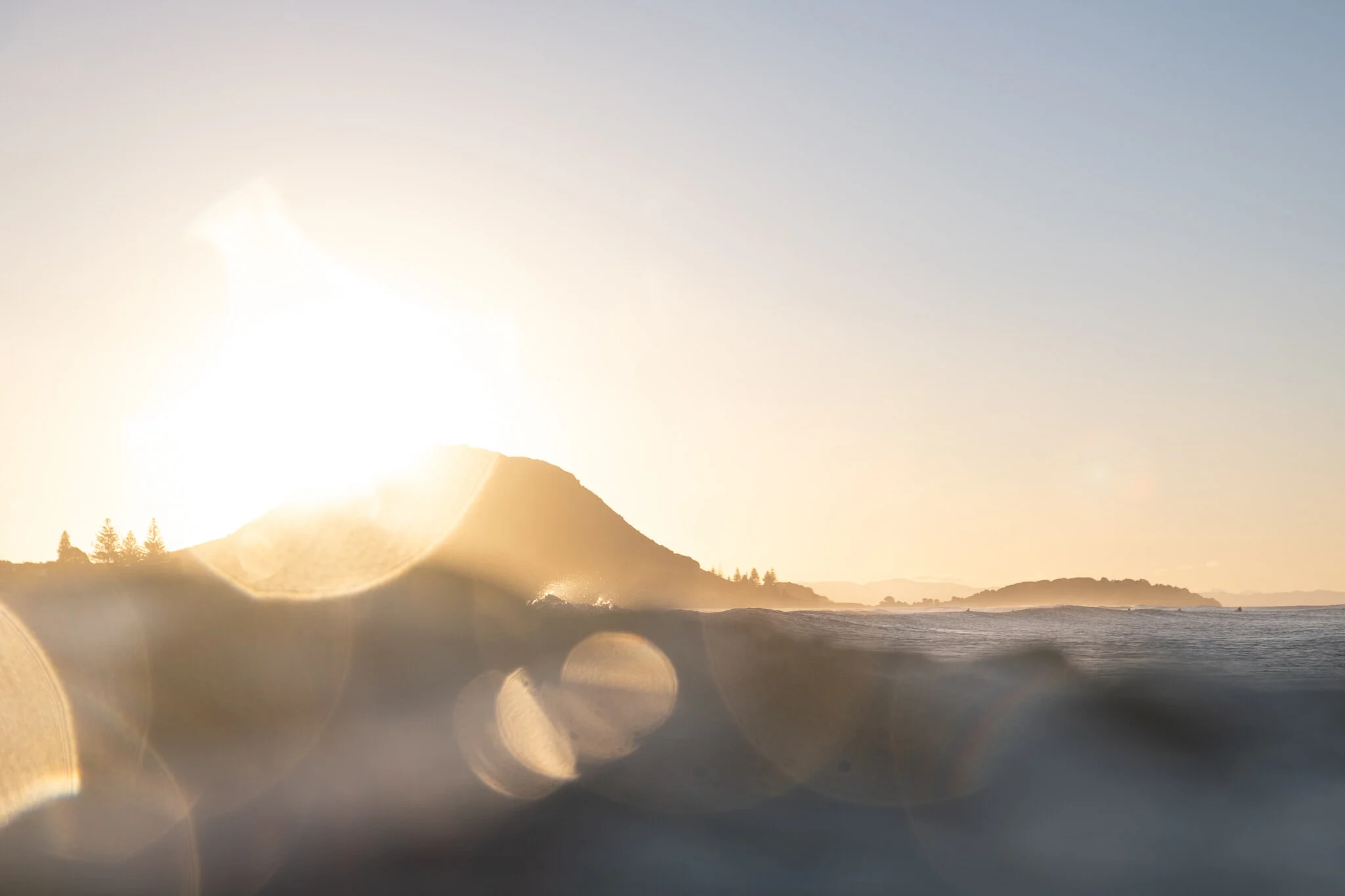 Mount Maunganui at sunset, featuring bokeh of the golden light over the ocean.