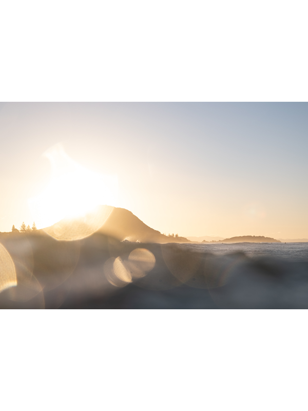 Mount Maunganui at sunset, featuring bokeh of the golden light over the ocean.