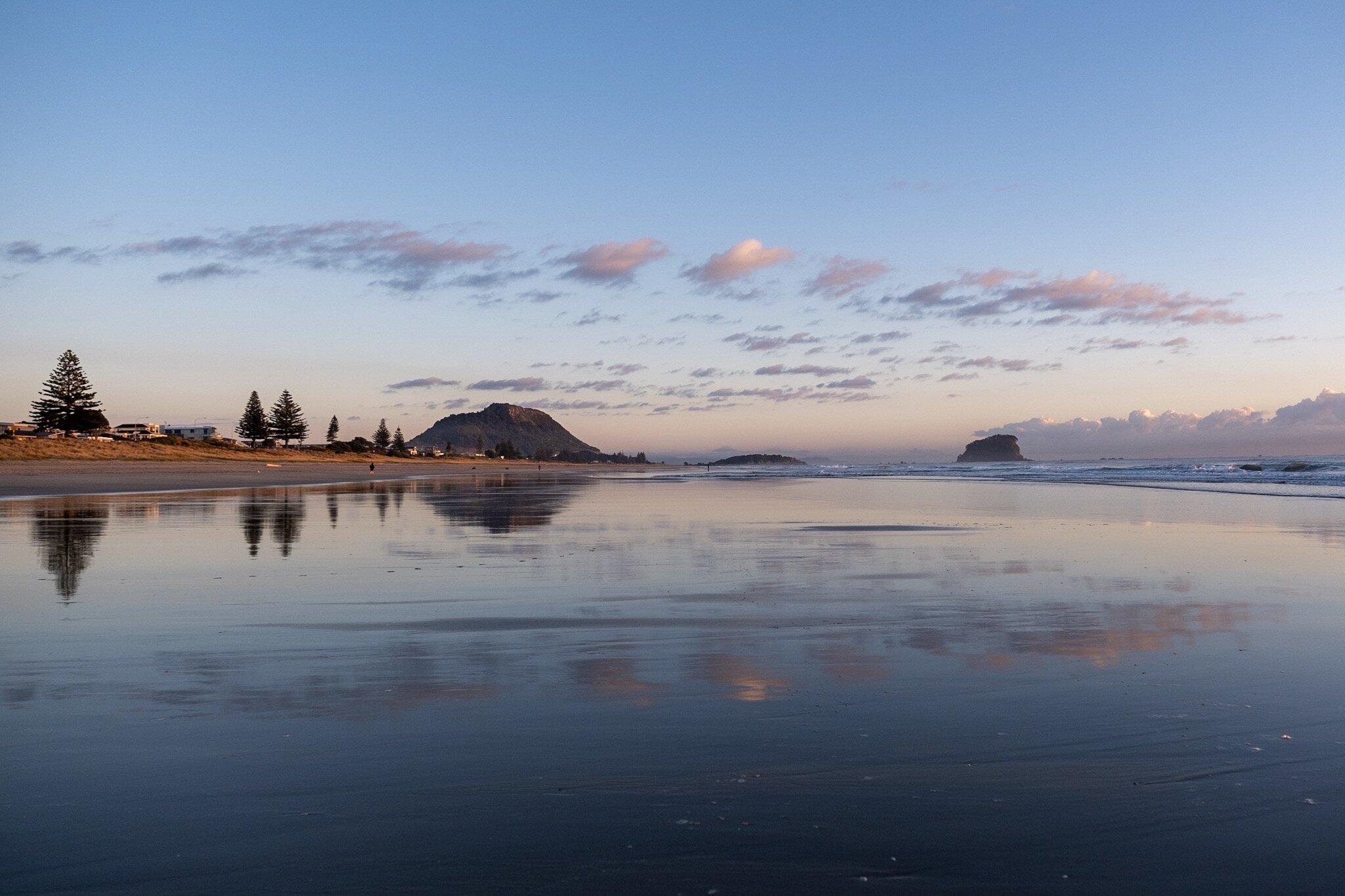 Mount Maunganui at low tide, with the whole beach scene reflected in the wet sand. The sky is a mixture of blues and purples with clouds stretching across the frame. Wide angle lens used to capture the expansive view. photo by Mount Maunganui ocean p