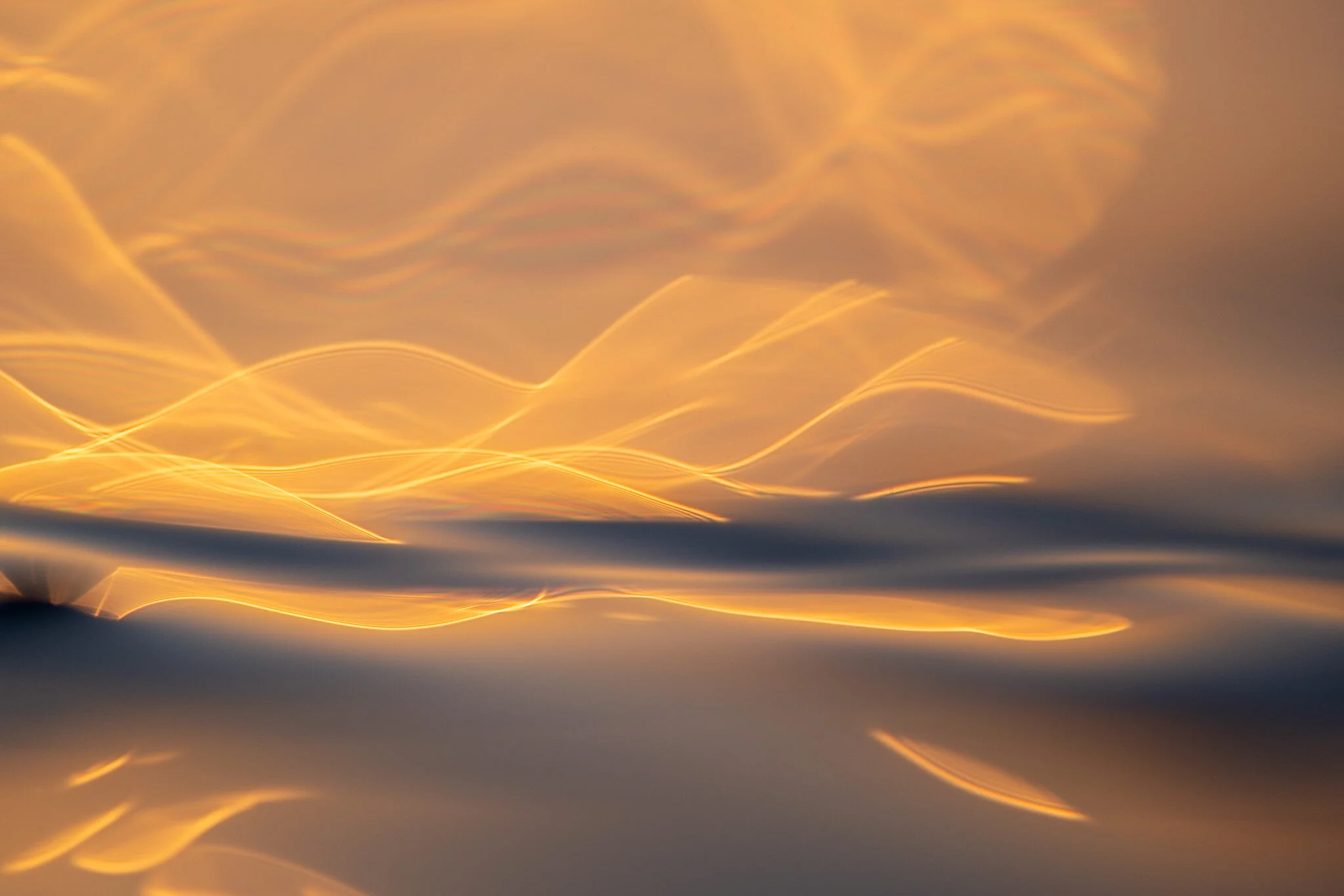 A mesmerizing abstract ocean photo taken at sunrise, using a macro lens to capture the dancing streaks of light on the water's surface. The photo is a stunning display of the ocean's beauty and abstract nature, captured by ocean photographer Lou Lou 